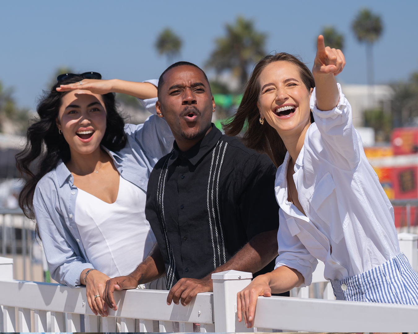 Three young people in the sun pointing at the sky enjoying Pacific Airshow.