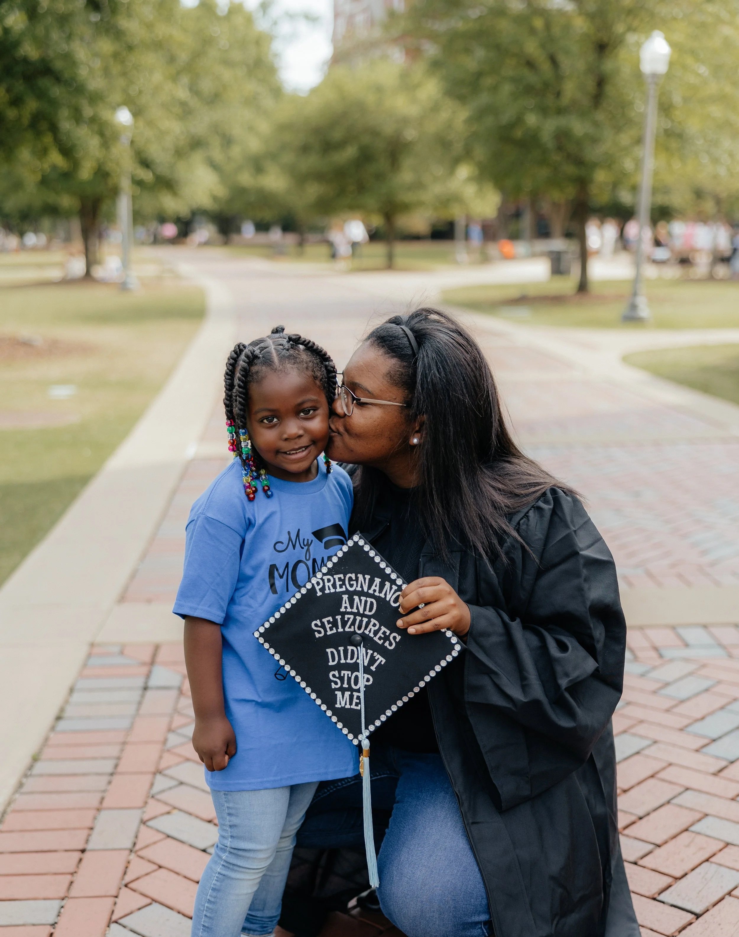 Baby Steps alumni Tyneshia with her child on graduation day and a cap that says pregnancy and seizures didn't stop me