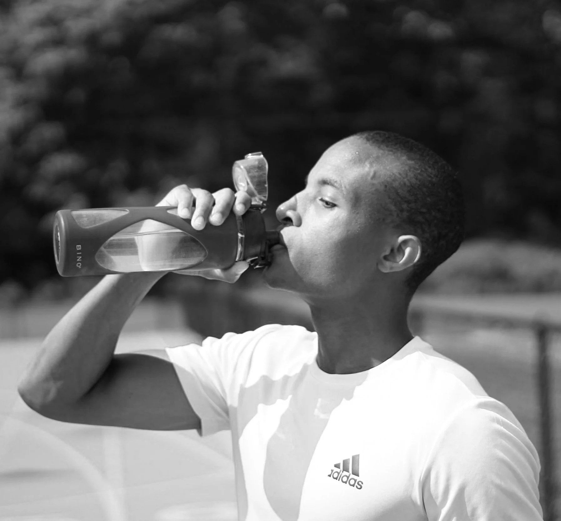 Young black man drinking water at a track. This examples man taking care of his physical health to reduce irritability.