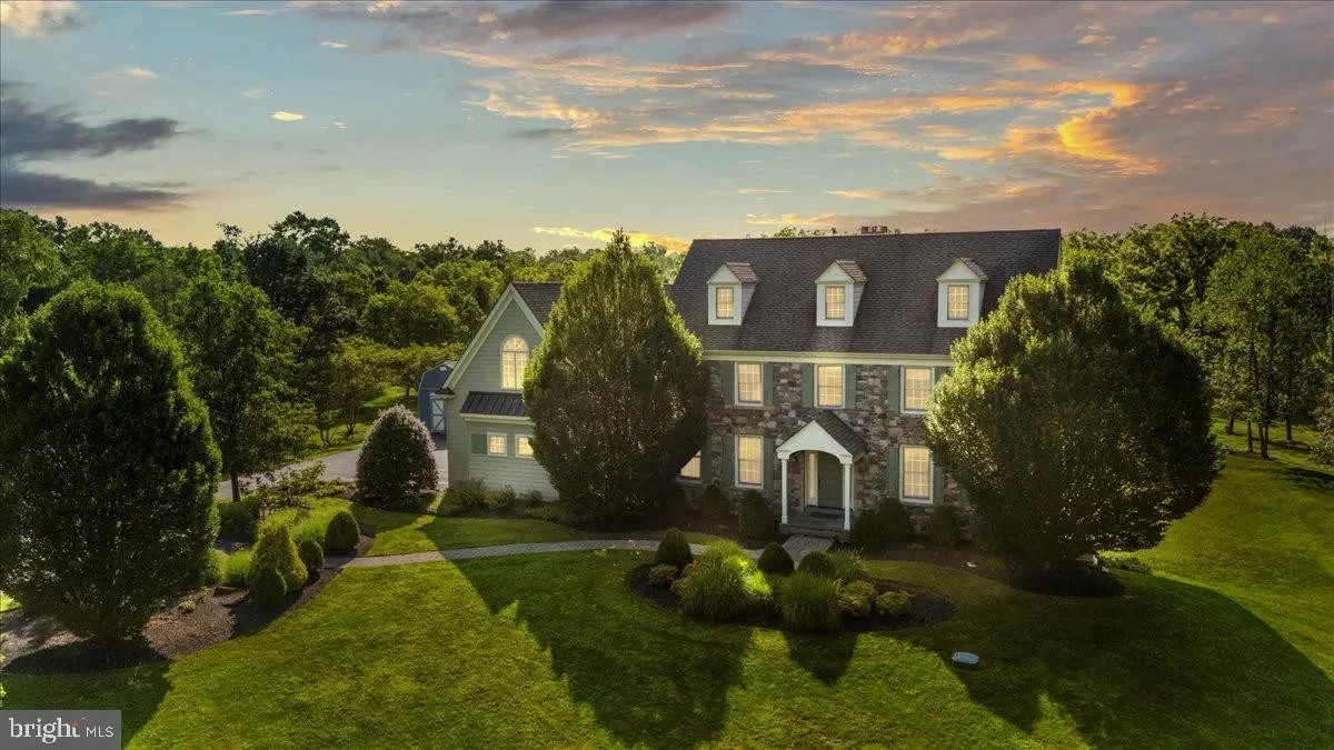 Large house with stone and light siding, surrounded by trees and a manicured lawn, during sunset.