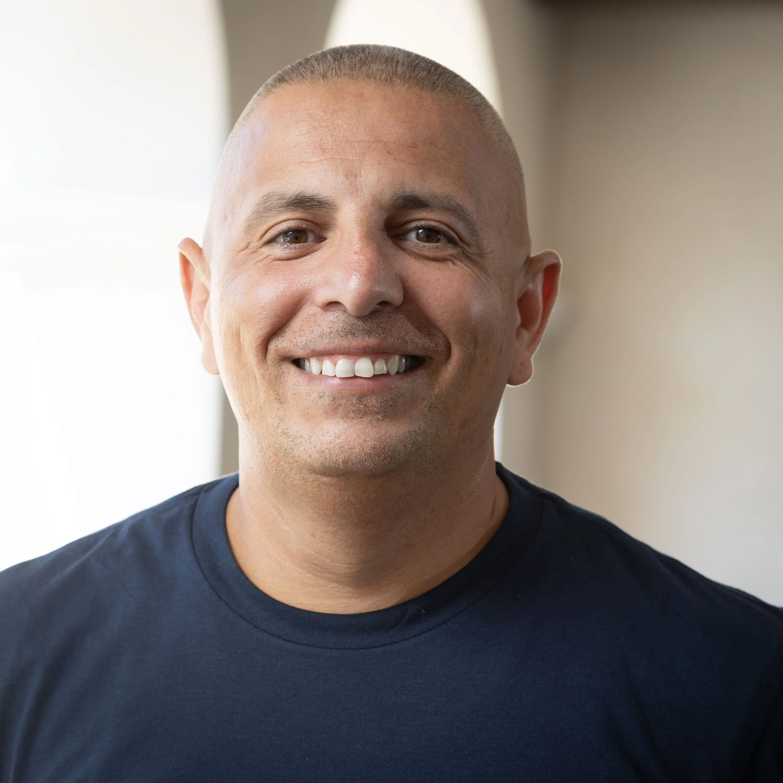A man with short hair and a slight smile, wearing a navy blue polo shirt with a 'California Republic Leadership Academy' logo, standing against a plain white wall.