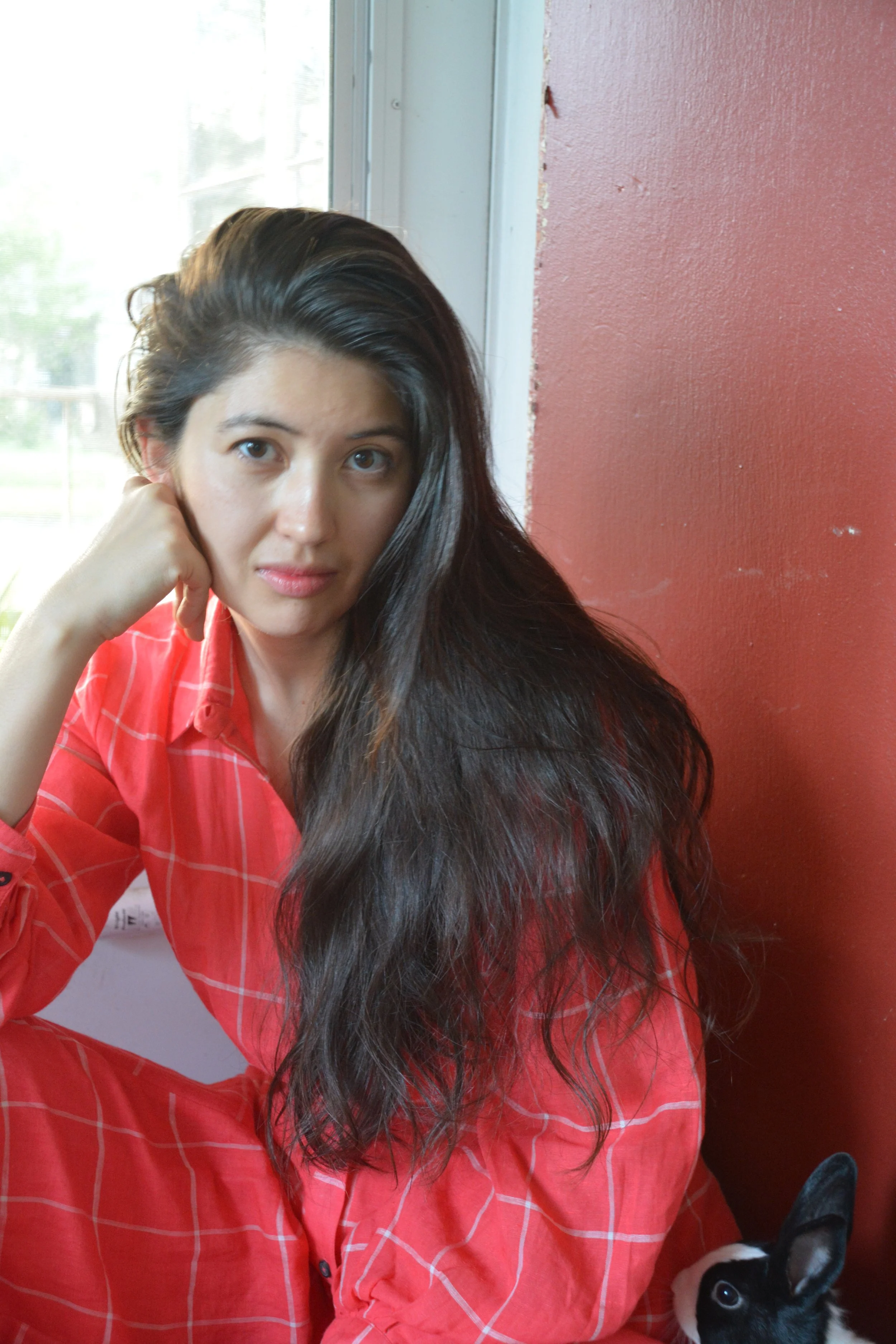 A headshot of Asa Drake in front of a red wall wearing a red and white plaid matching set