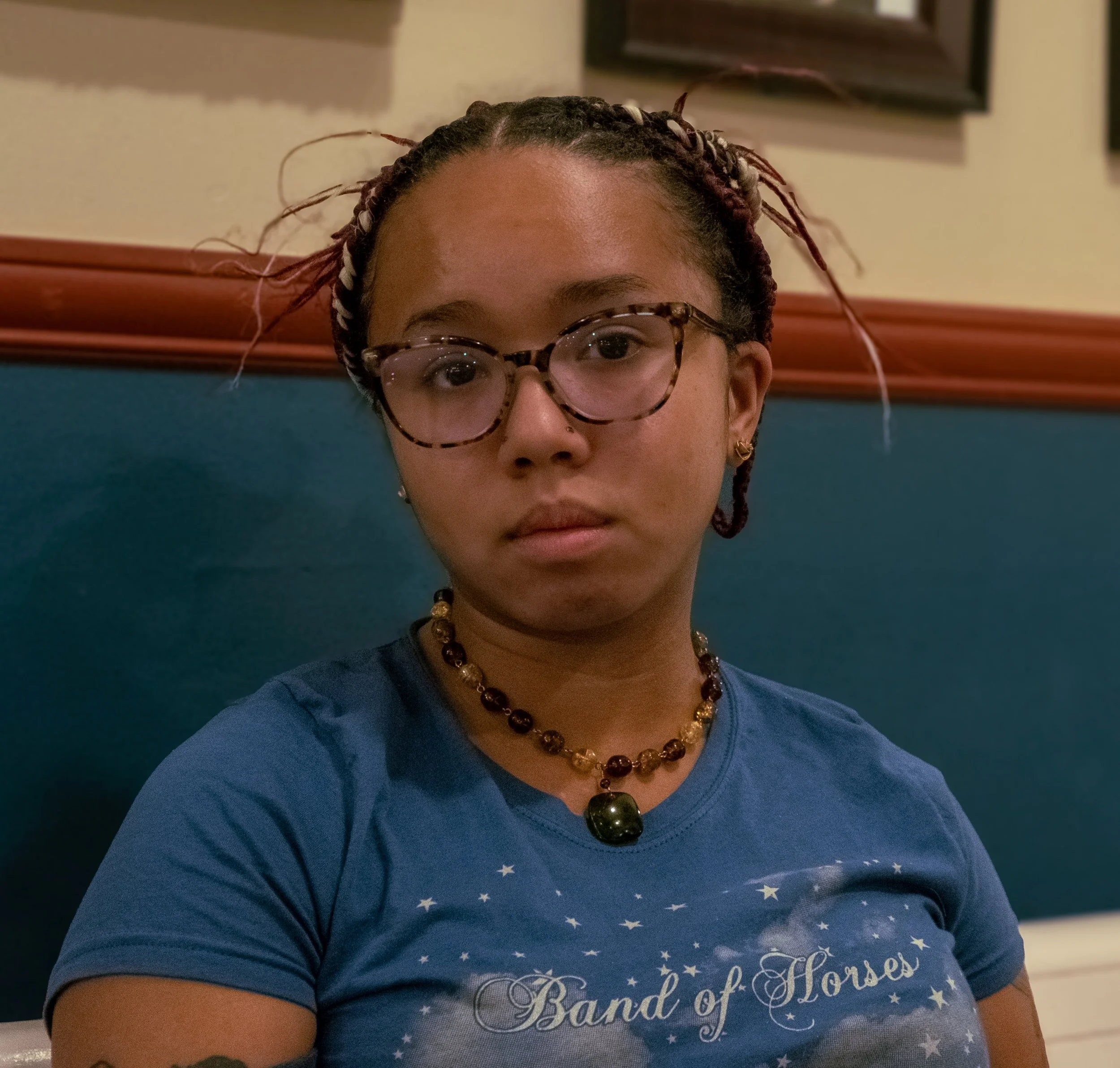 A headshot of Bella Gordo, wearing a blue shirt and brown necklace