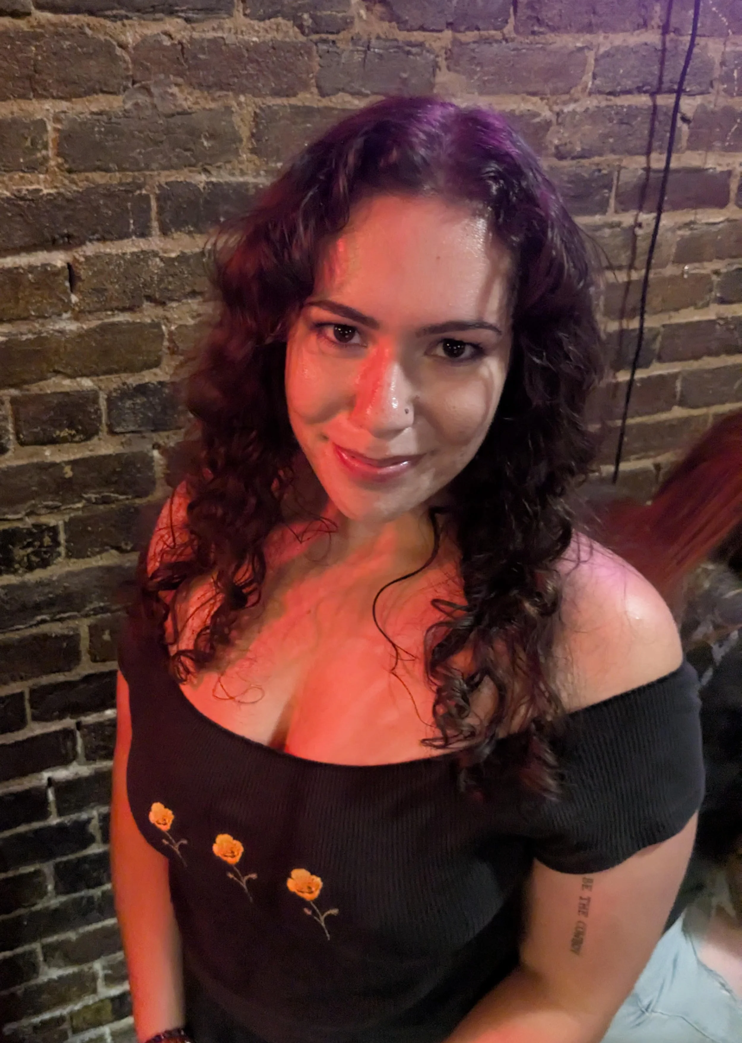 A headshot of Shira Haus in a black top standing in front of a brick wall