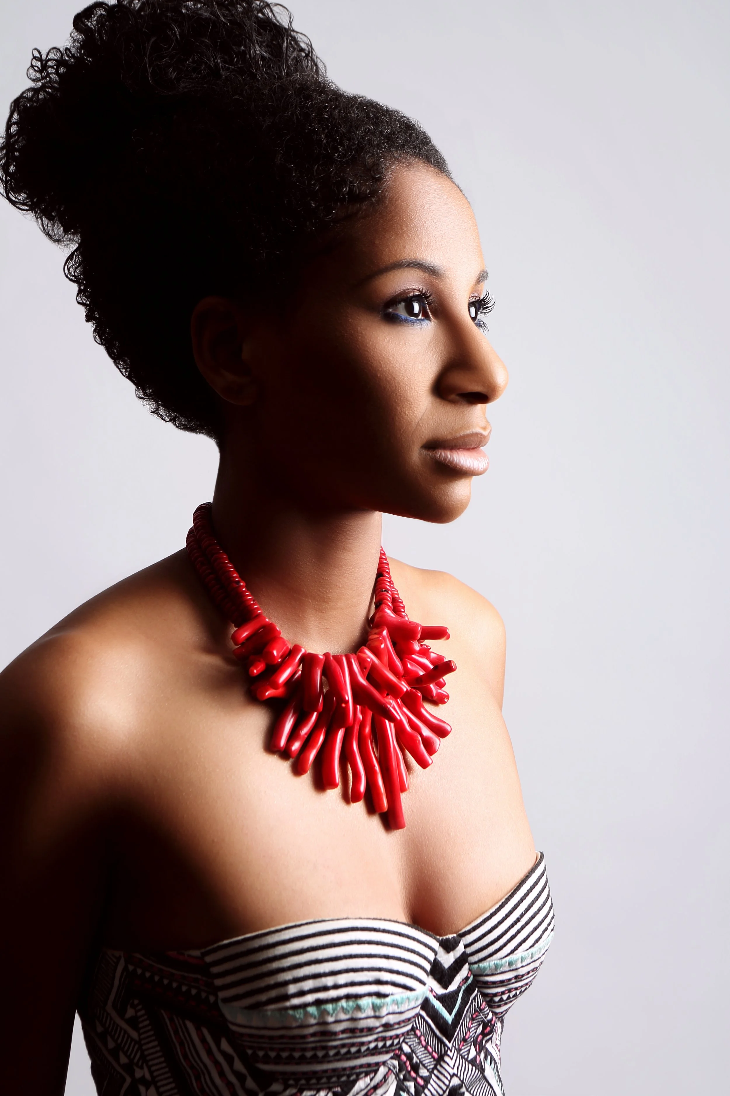 Photo portrait of Alison C. Rollins with her hair up in a bun, a red statement necklace. She is looking to the right of the camera.