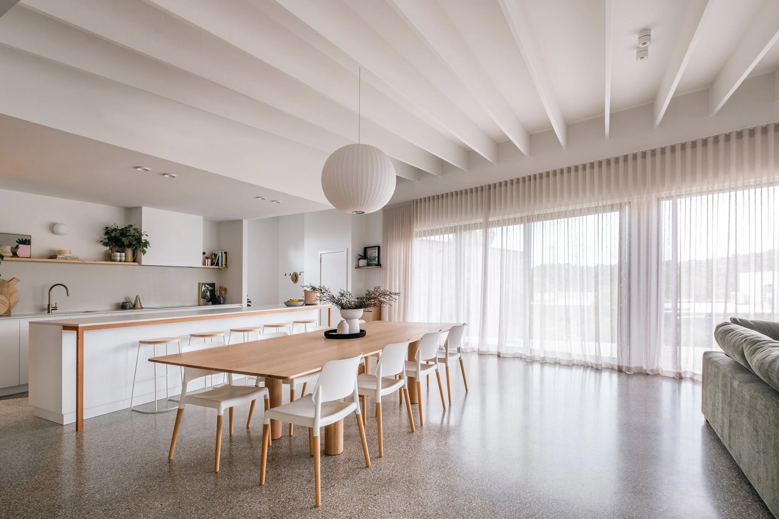 Donvale House open-plan kitchen and dining with long timber table and sheer curtains