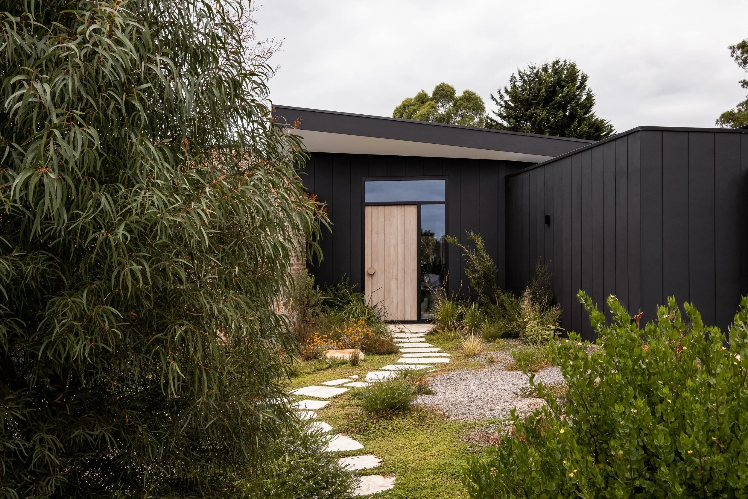 Donvale House black-clad entry with timber door and stepping-stone path through garden