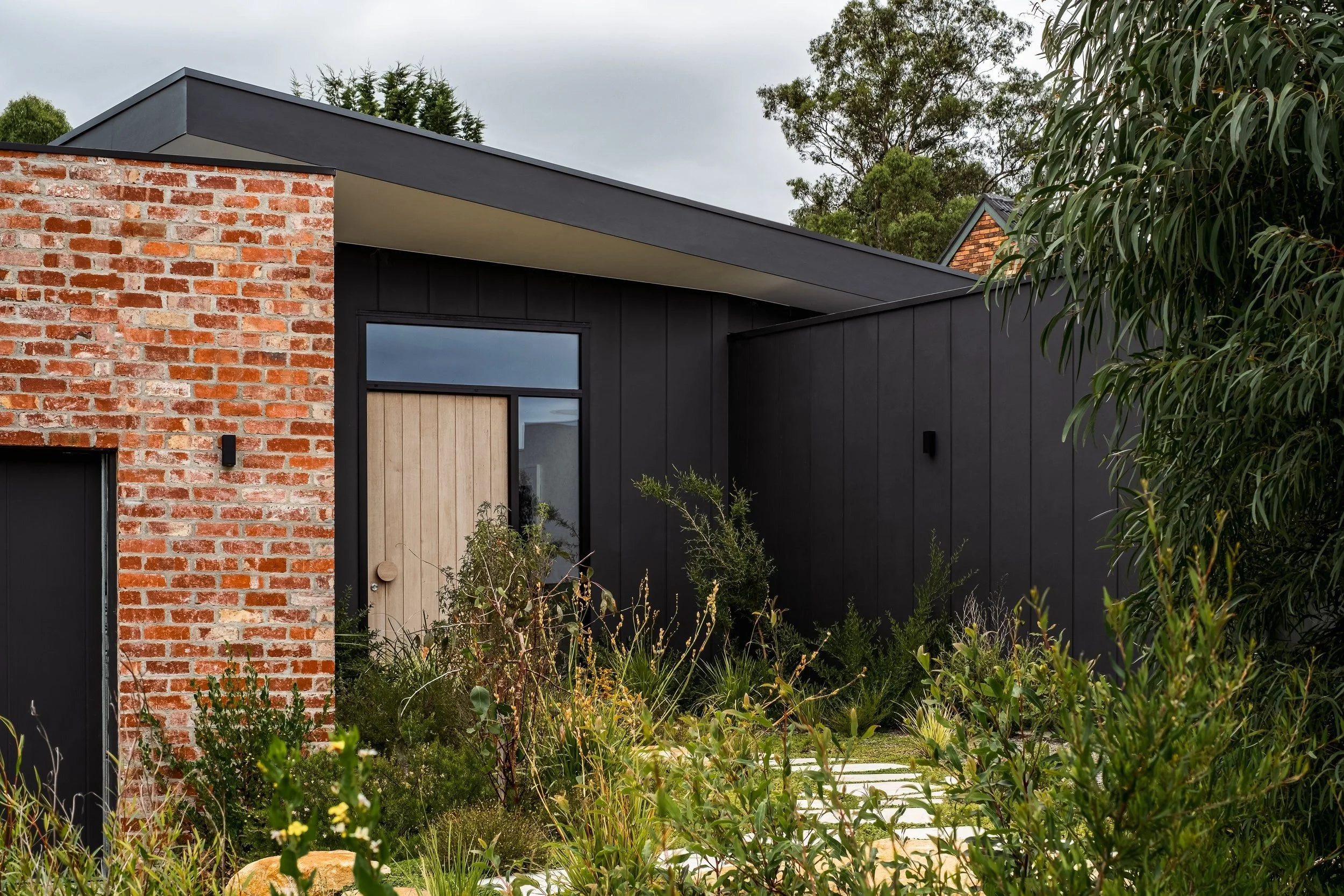 Donvale House entry with red brick wall, black cladding and timber door