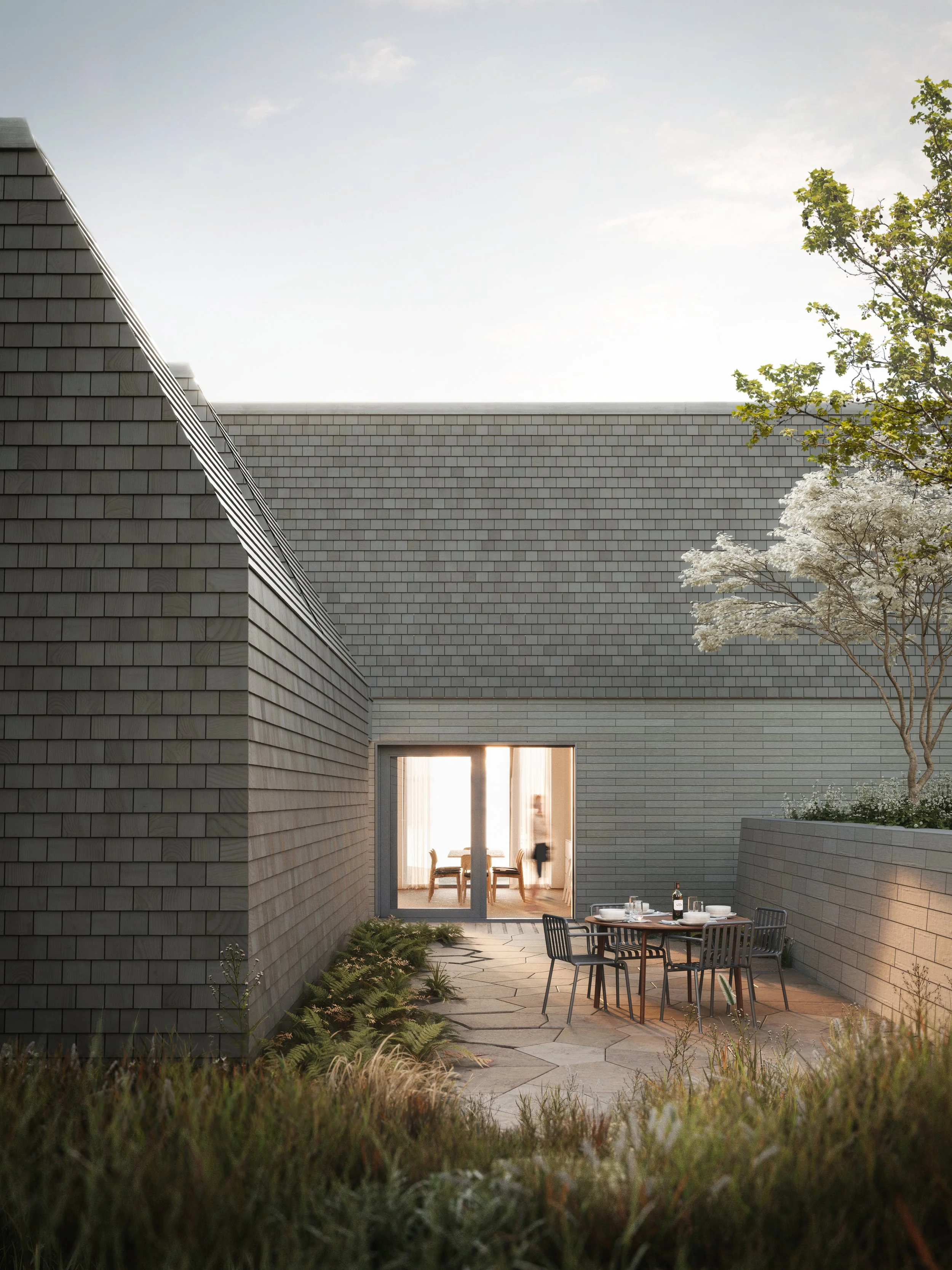 Exterior courtyard of a custom home in Cape Breton, featuring local stone, cedar shingles, natural materials, and warm evening light