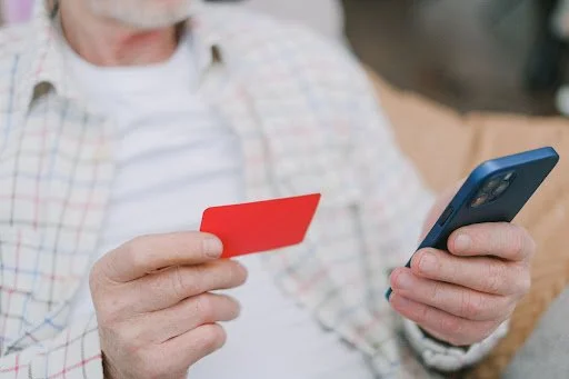 Man in checked shirt holding a blank red credit card and a mobile phone