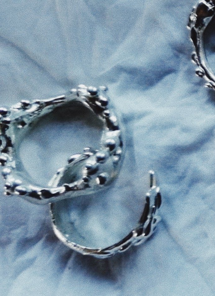 Close-up of silver hoop earrings with textured design on a light blue fabric background.