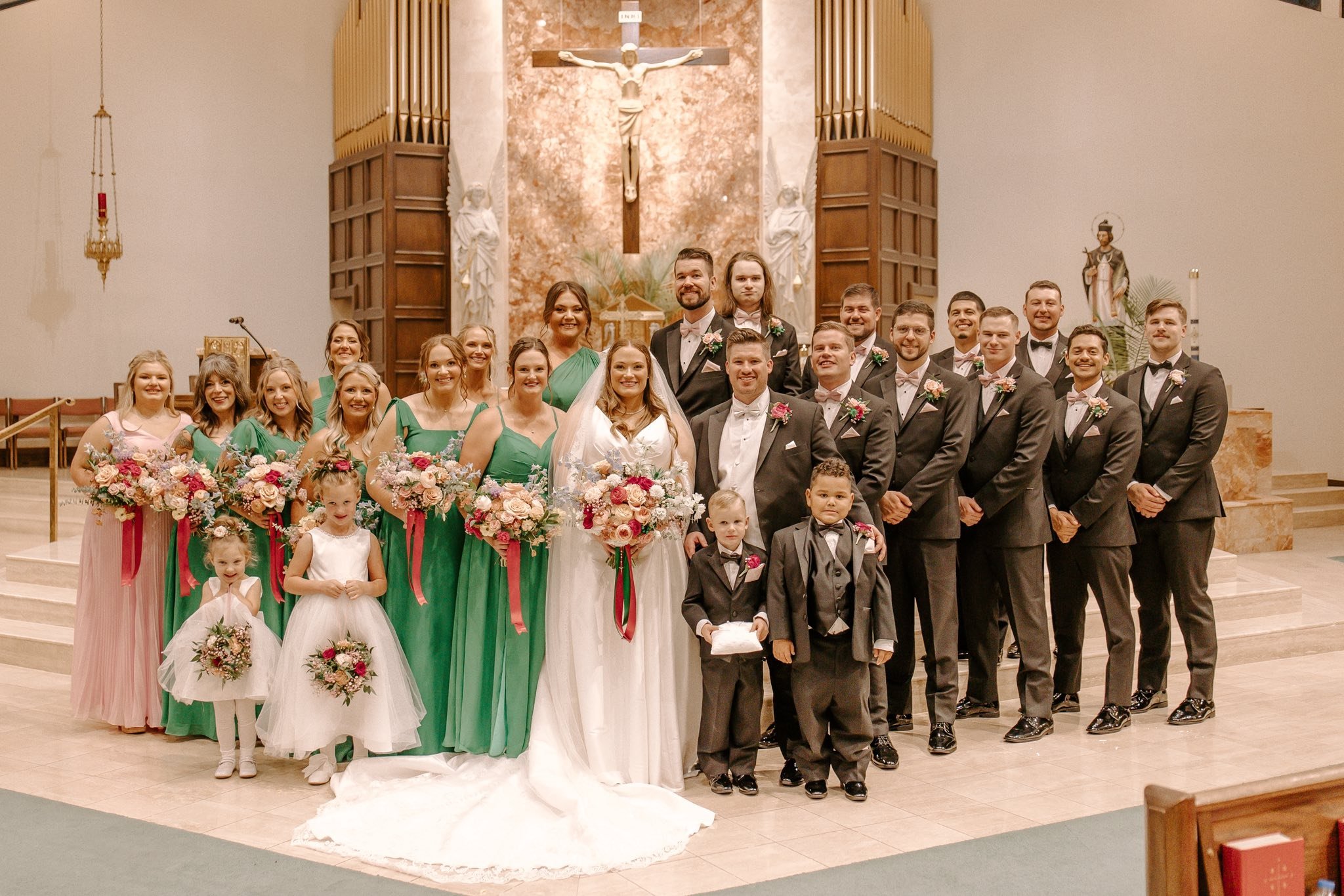 Bride and groom standing with their wedding party at the altar during a Catholic wedding ceremony in Oklahoma, surrounded by family, florals, and formal attire.