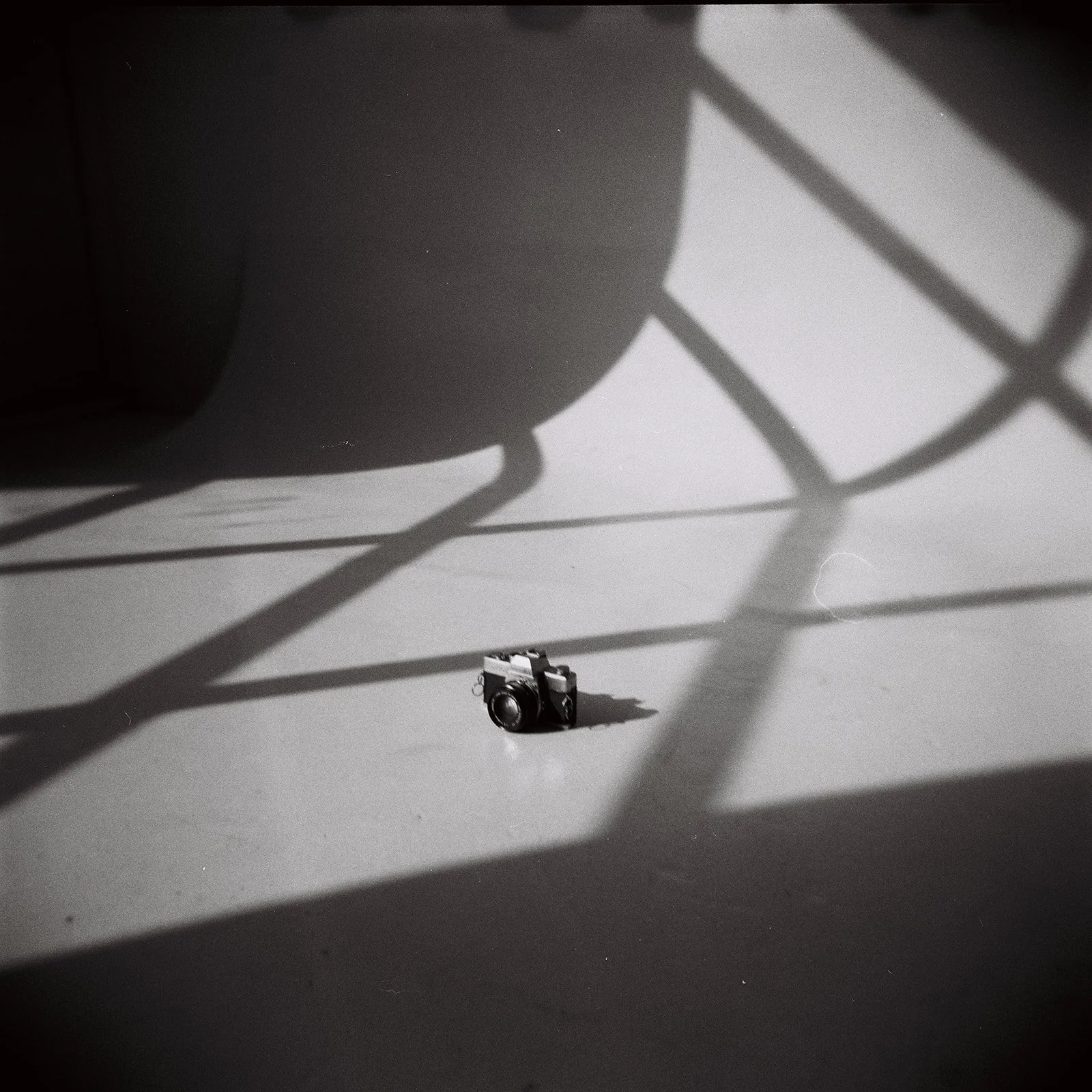 A small camera on a flat surface, casting shadows of a skateboard and chairs on the wall.