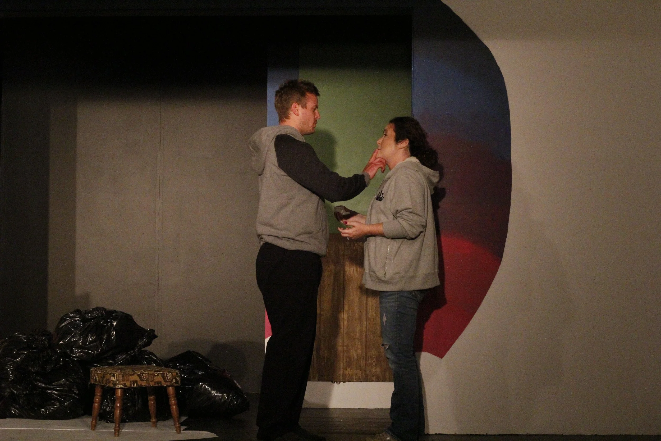 A man touching a woman's chin as they stand facing each other on a stage.