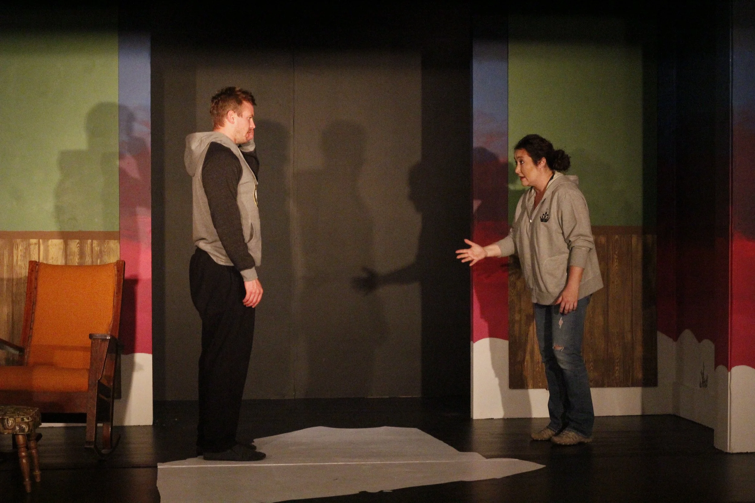 Two women are on a stage, with one standing and the other gesturing towards her, engaged in a conversation or performance.