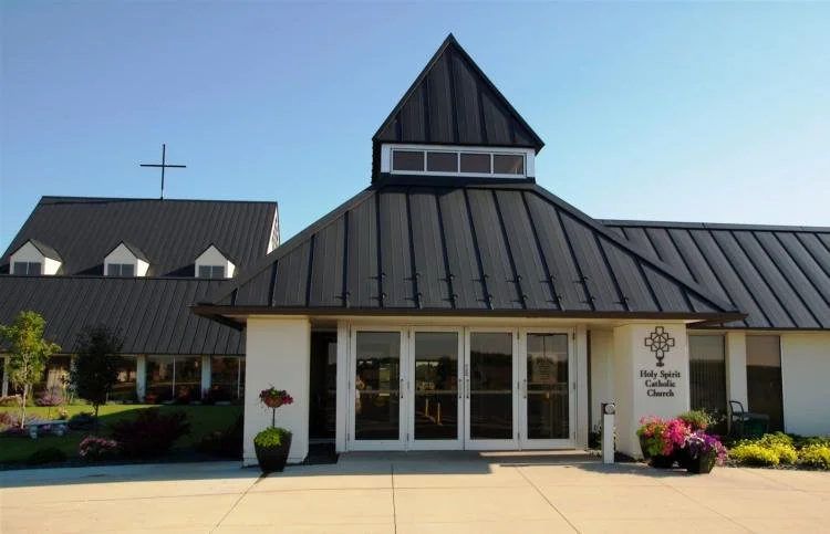 Modern church building with dark metal roof, large windows, and cross