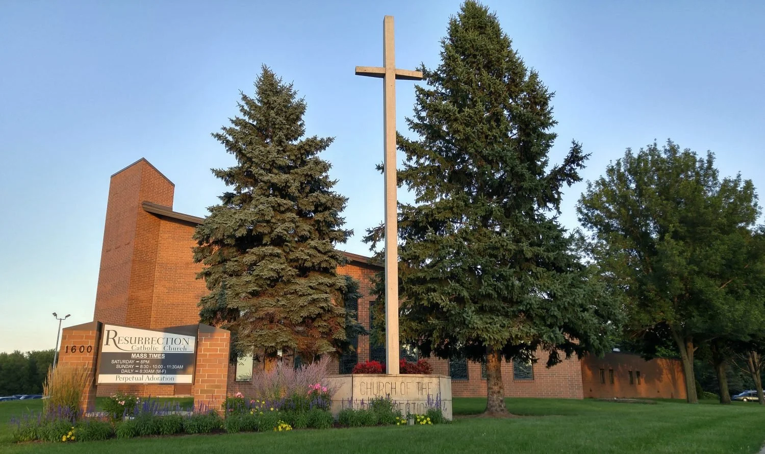 Resurrection Catholic Church with large cross, surrounded by trees and greenery.
