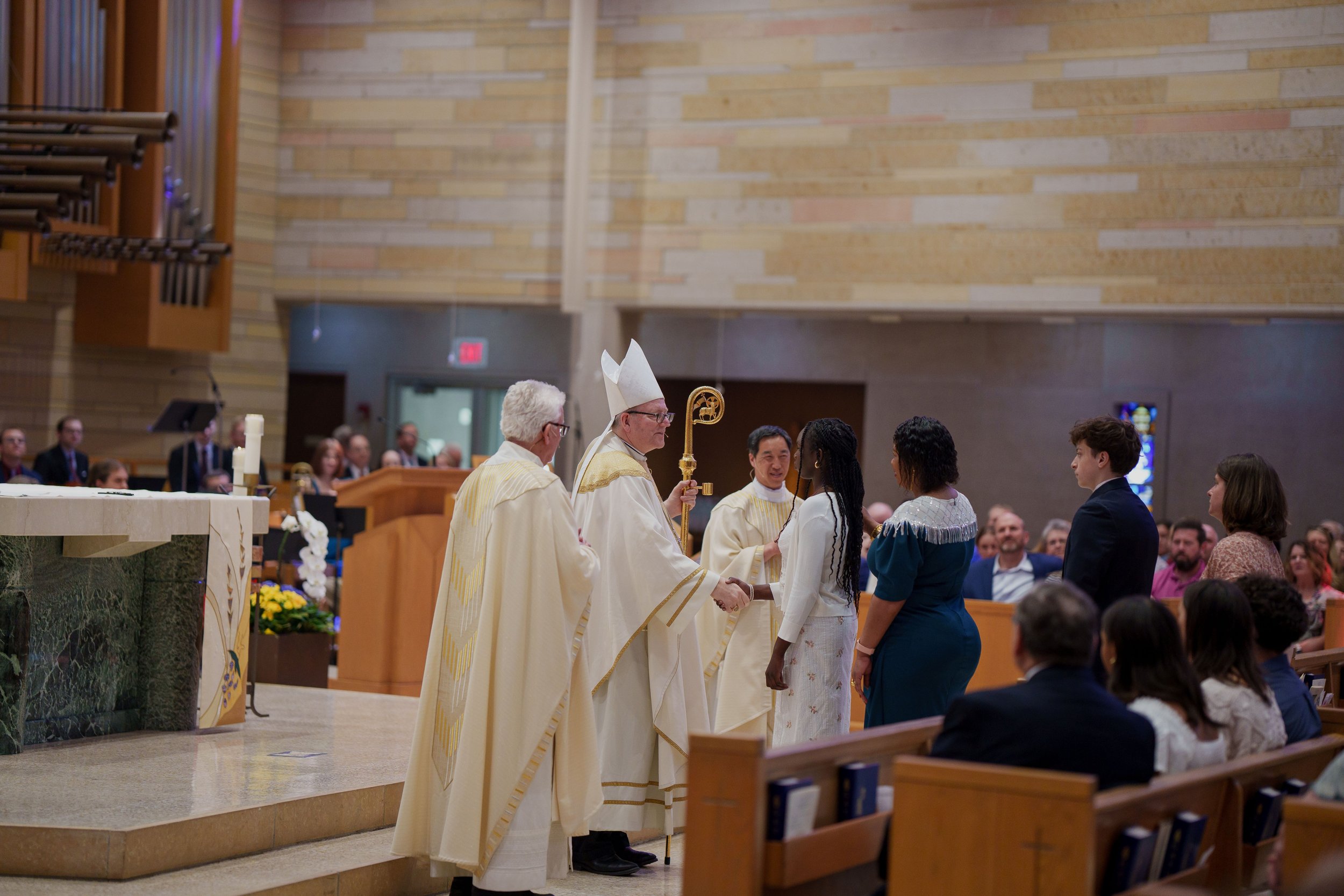 Bishop Confirms a student with priest standing on the side