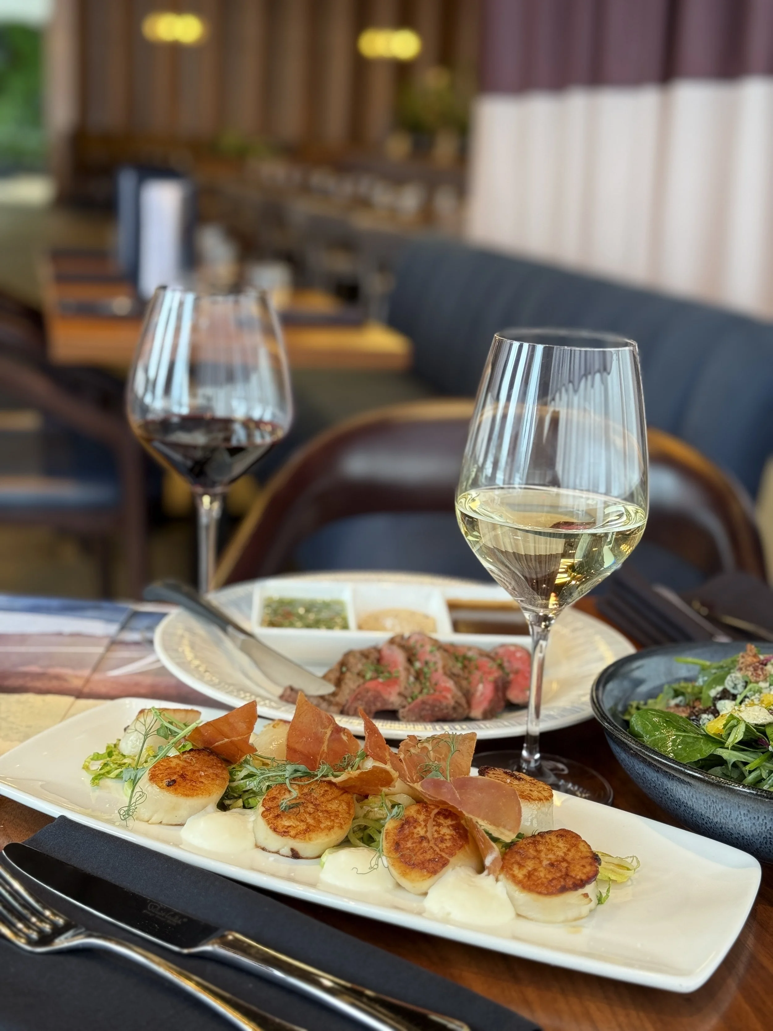 A place setting at Alara restaurant in Cincinnati and a white plate with scallops, glass of white wine, glass of red wine, and a steak.