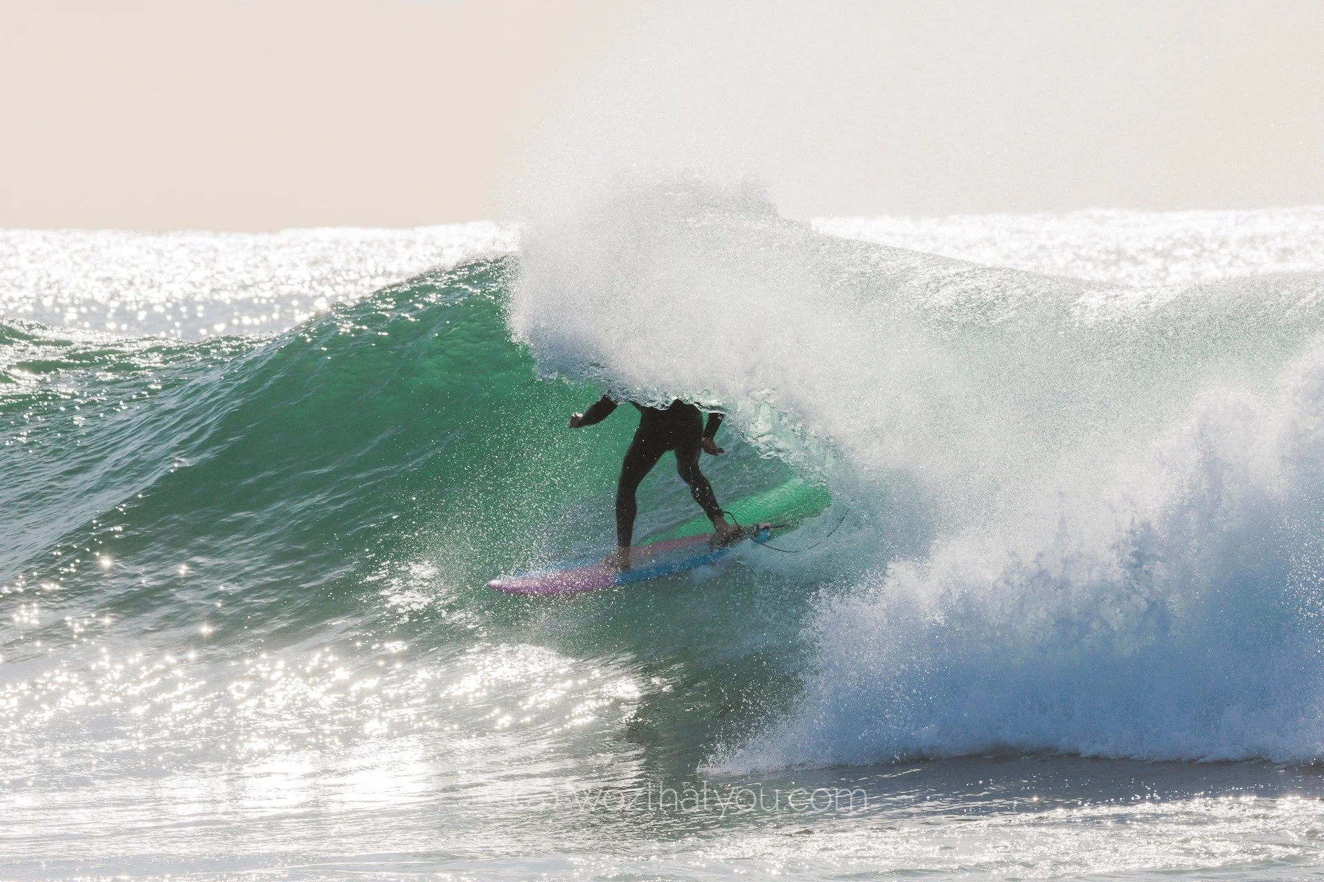 Surfer riding inside the barrel of a large wave with sunlight reflecting off the water.