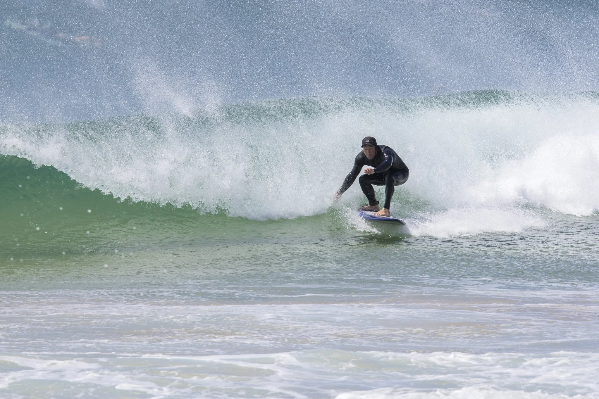 A person in a black wetsuit surfing on a surfboard on a green wave in the ocean.