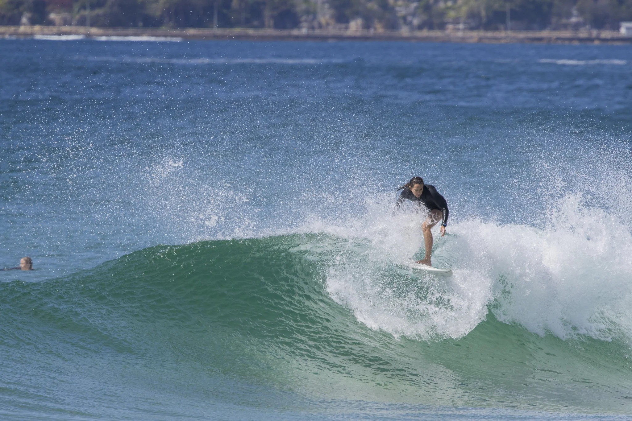 A woman surfing on a wave in the ocean, with another person swimming in the background.
