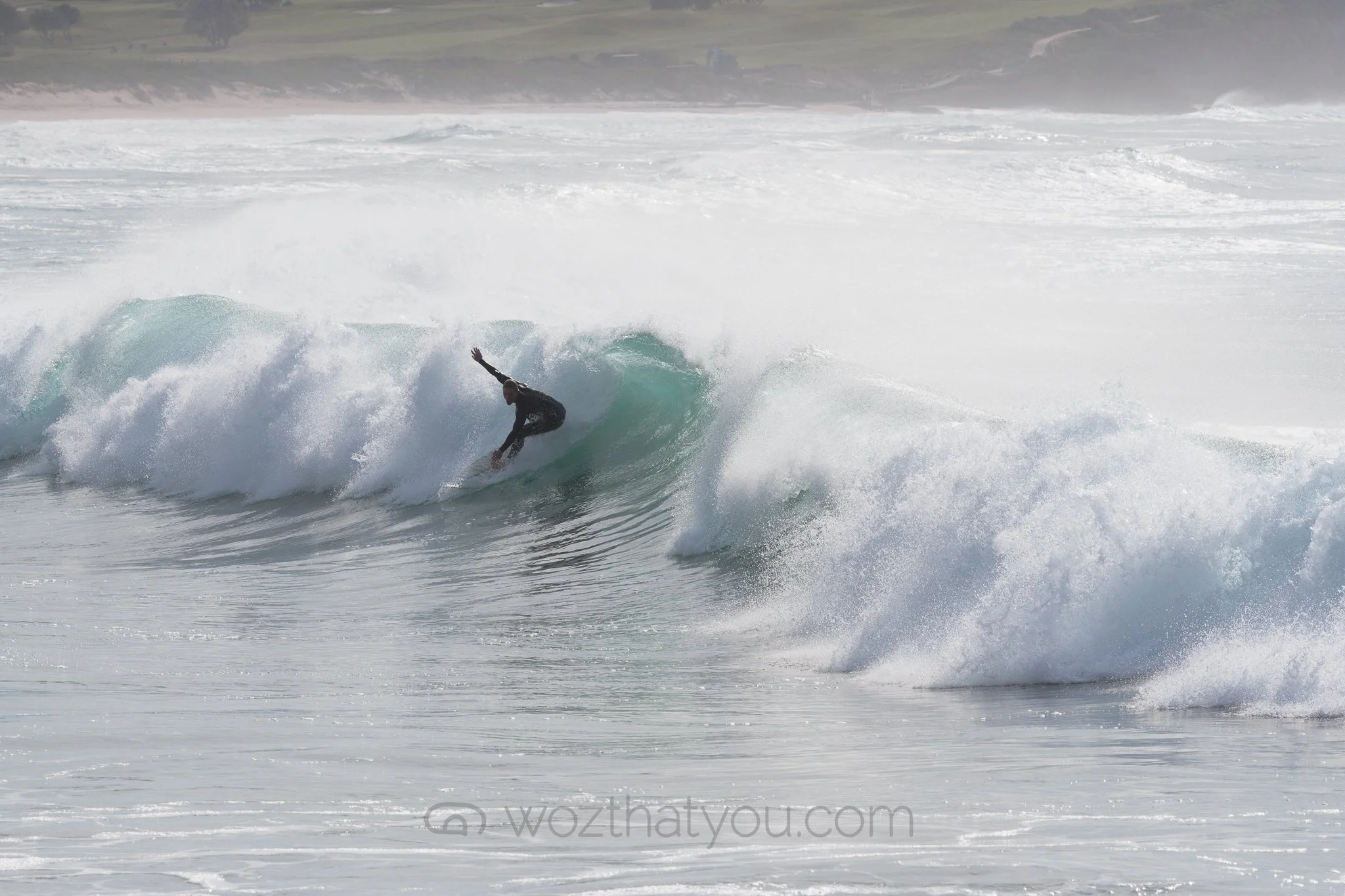 A person surfing on a wave in the ocean during daytime with cloudy sky.