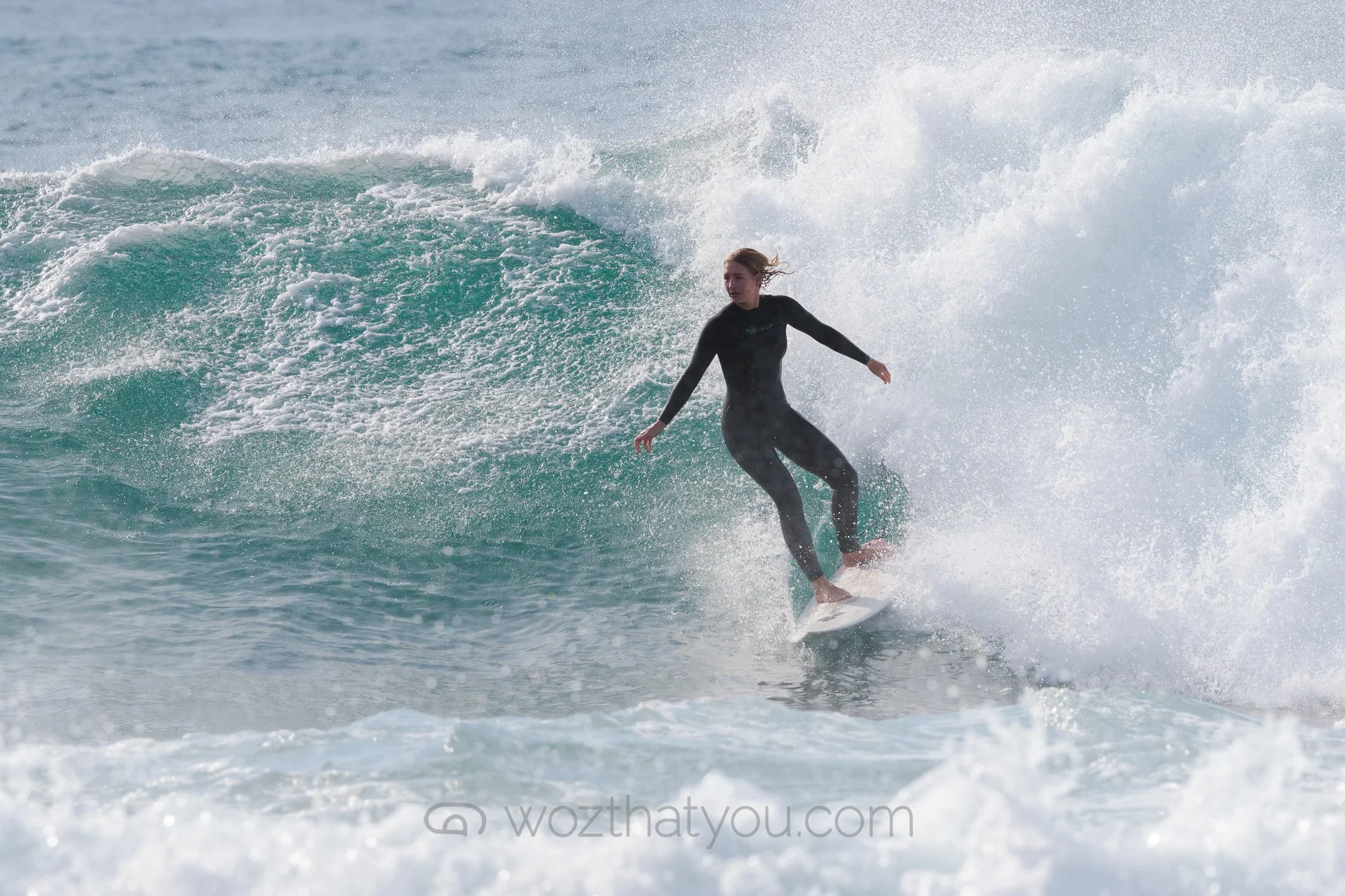 A woman in a black wetsuit surfing on a wave in the ocean.