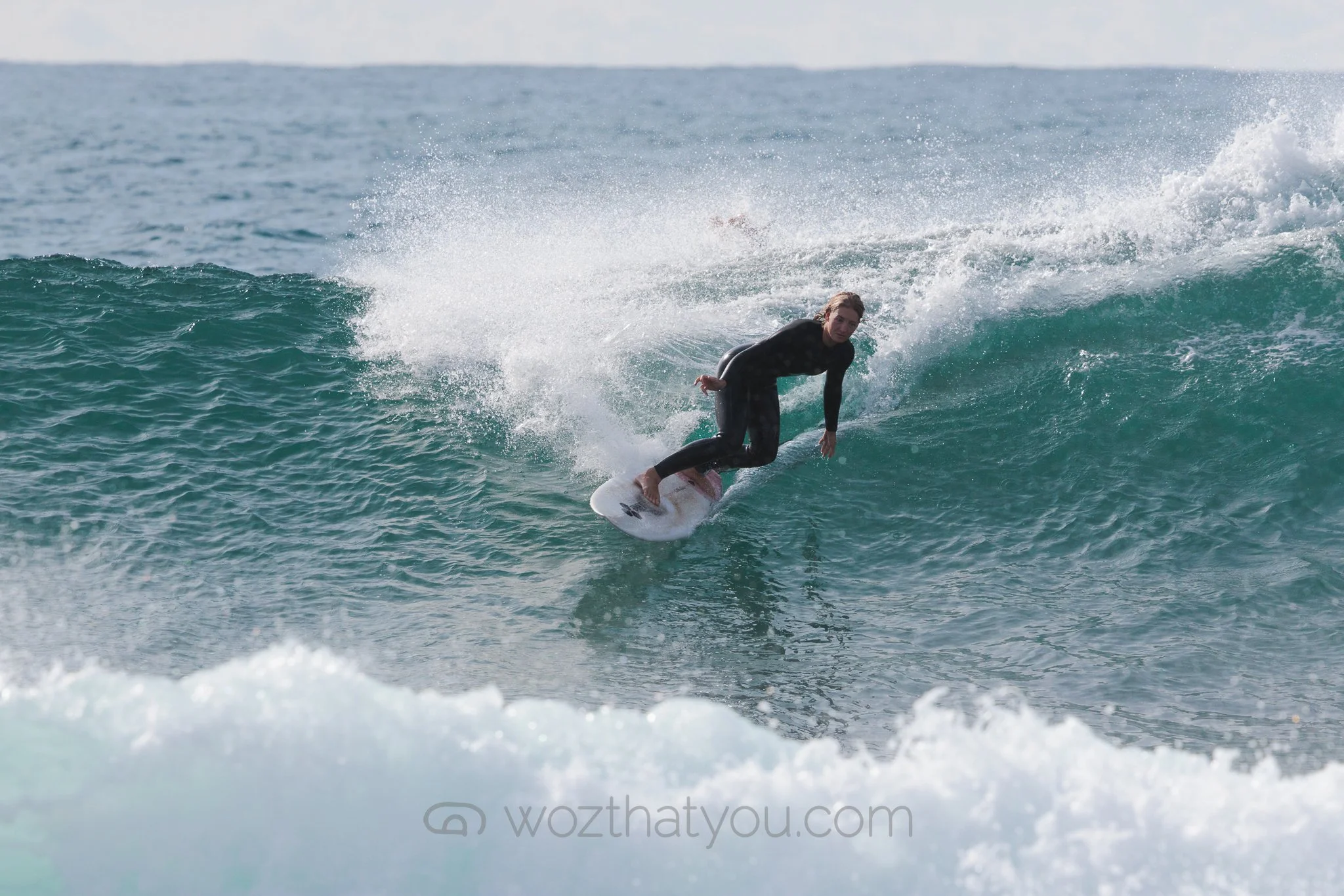 A woman surfing on a wave in the ocean, wearing a black wetsuit.