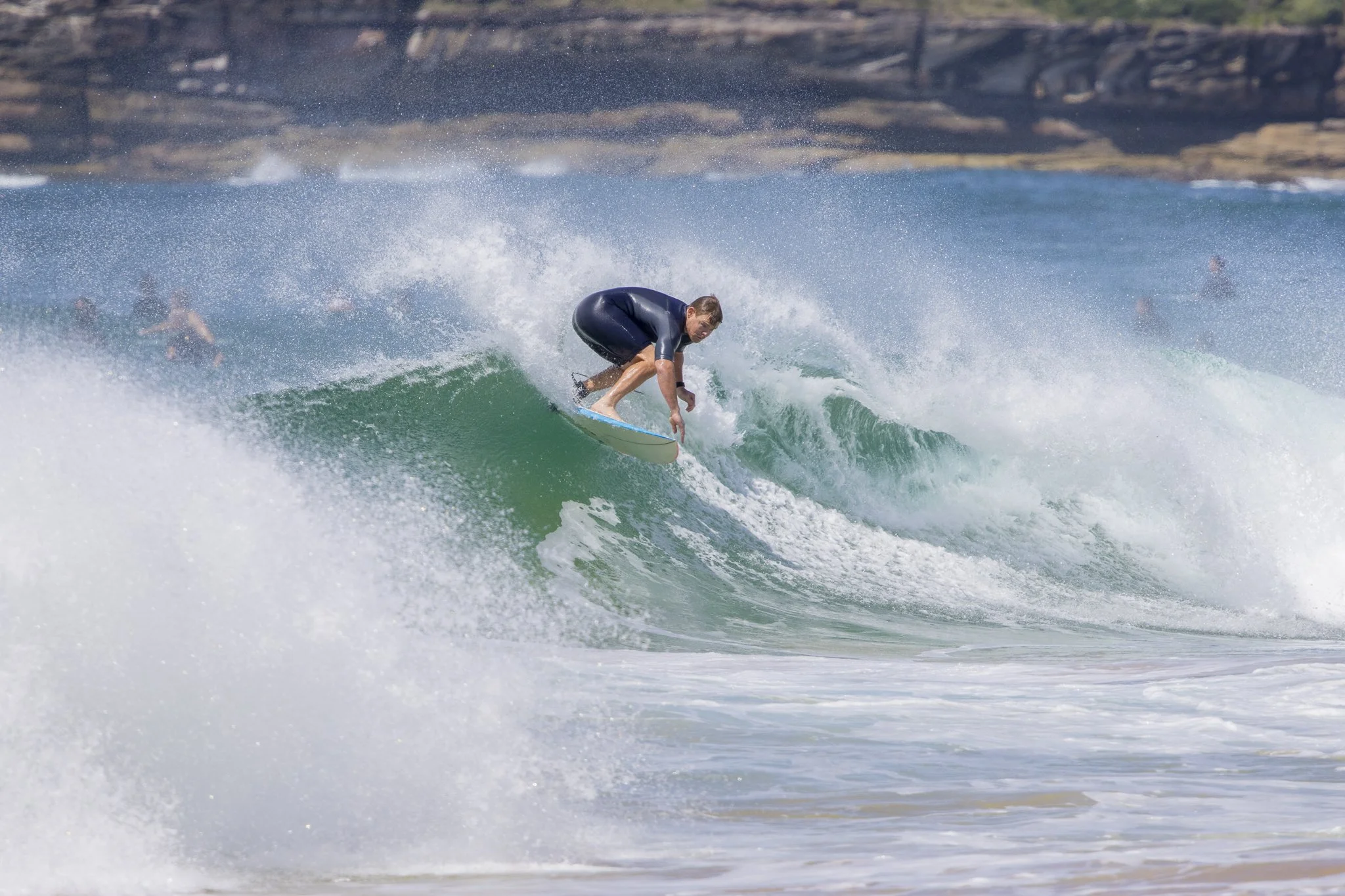 A man surfing on a green wave at the beach with rocky cliffs in the background.