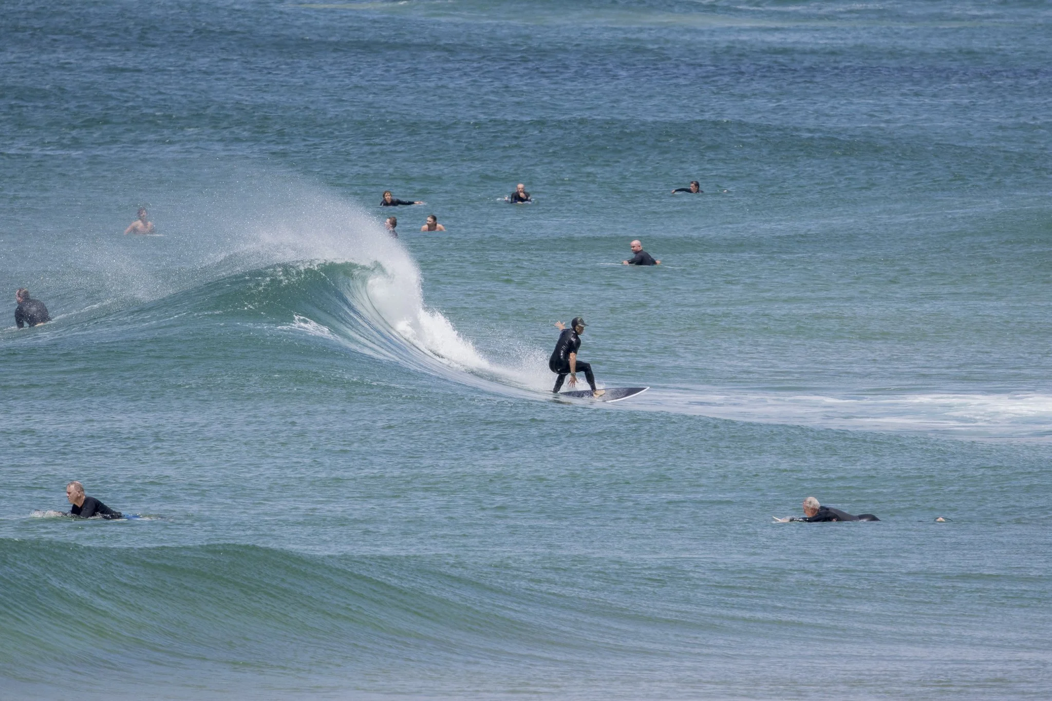 A person surfing on a wave with several people swimming and floating in the water nearby.
