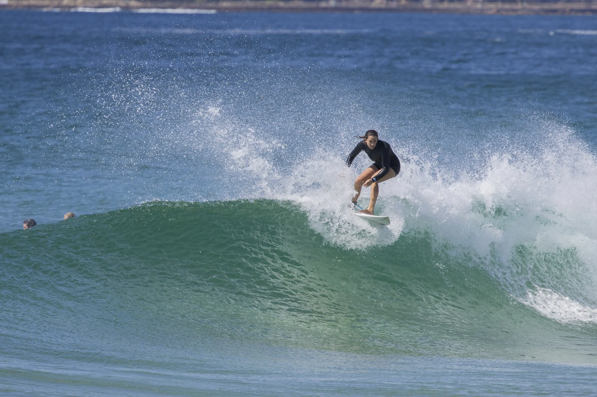 A woman surfing on a wave in the ocean, wearing a black wetsuit.
