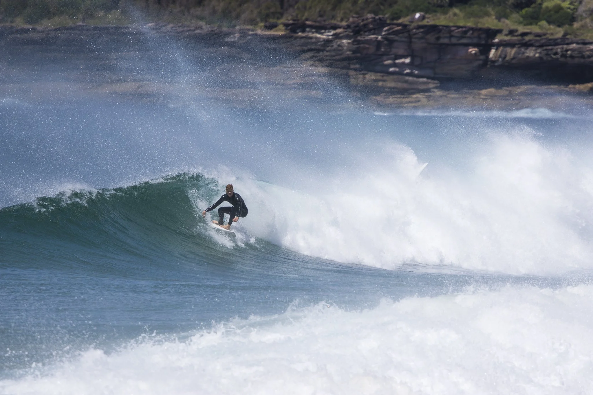 A surfer riding a wave in the ocean near a rocky shoreline.