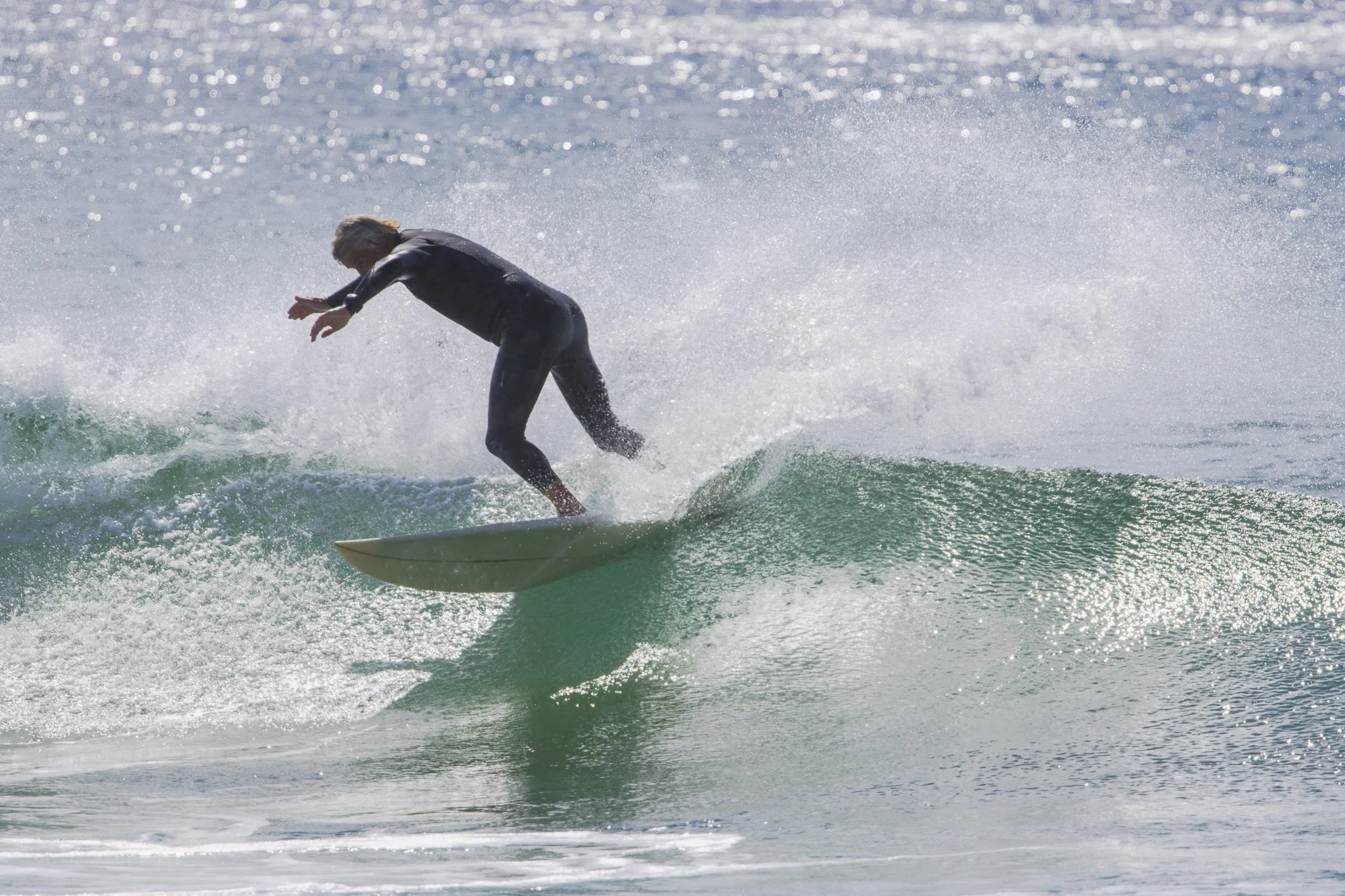 A person surfing on a wave in the ocean, wearing a black wetsuit.