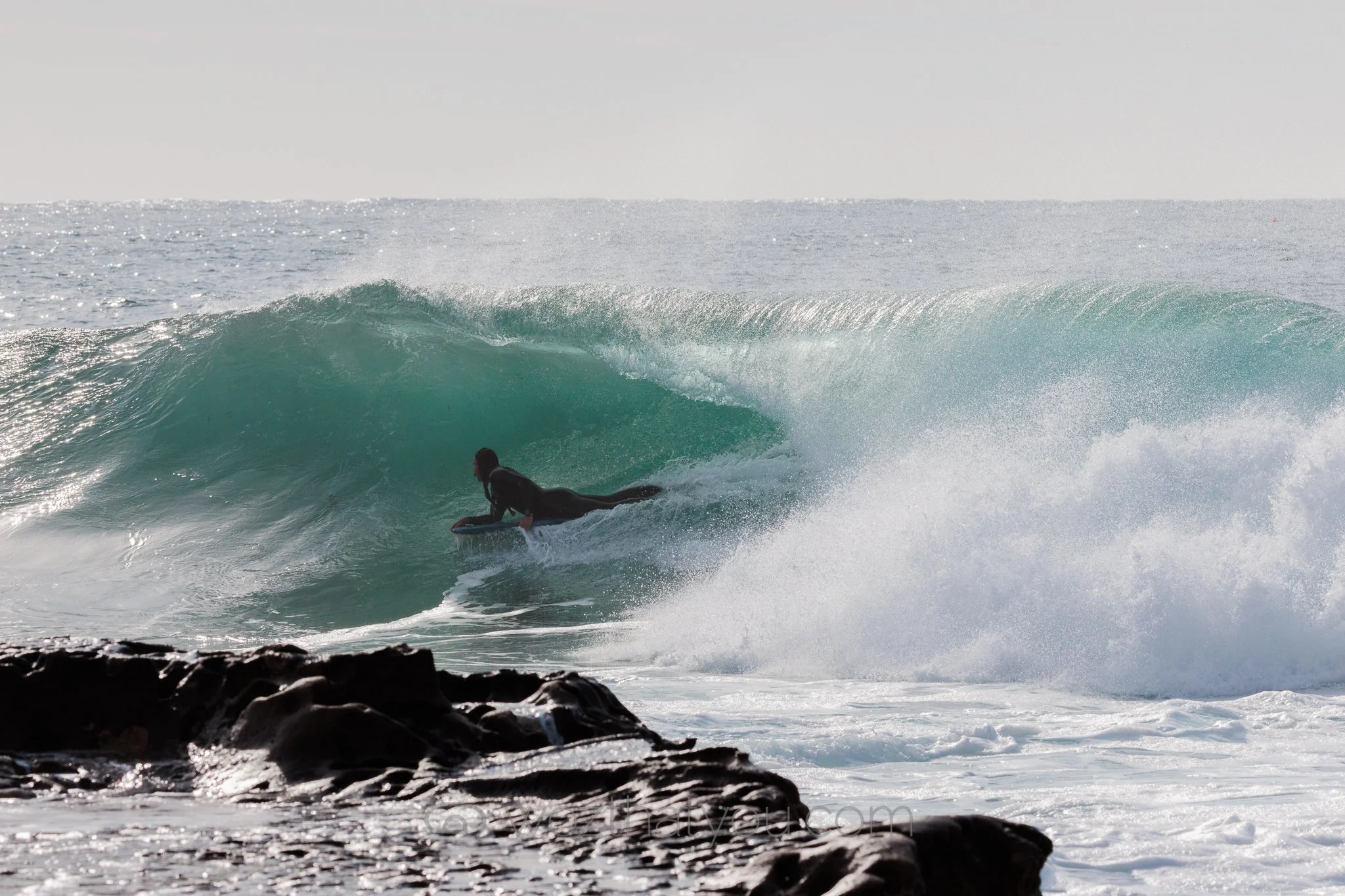A person surfing on a wave near rocks in the ocean.
