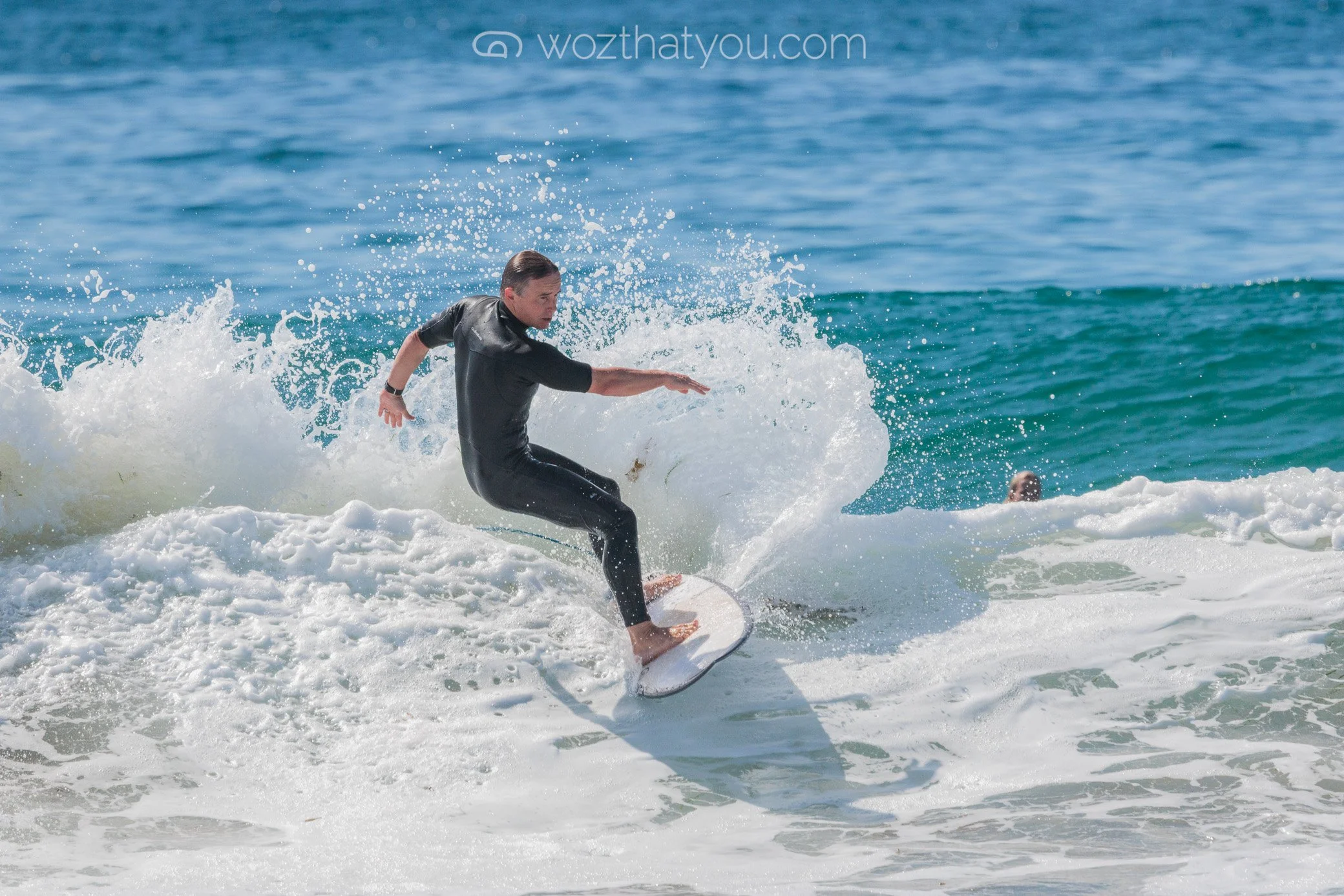 A person surfing on a wave in the ocean wearing a black wetsuit.