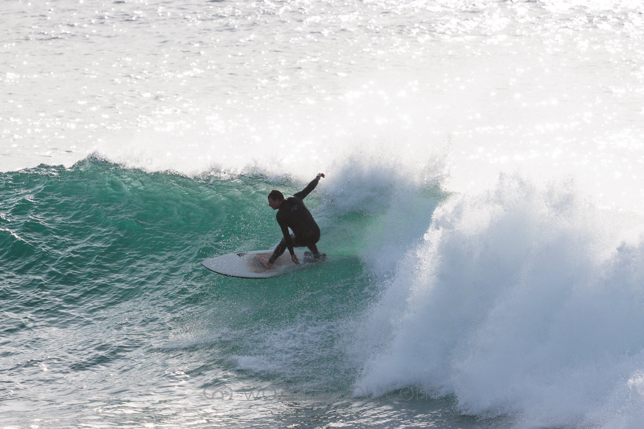A person surfing on a wave in the ocean, wearing a black wetsuit.