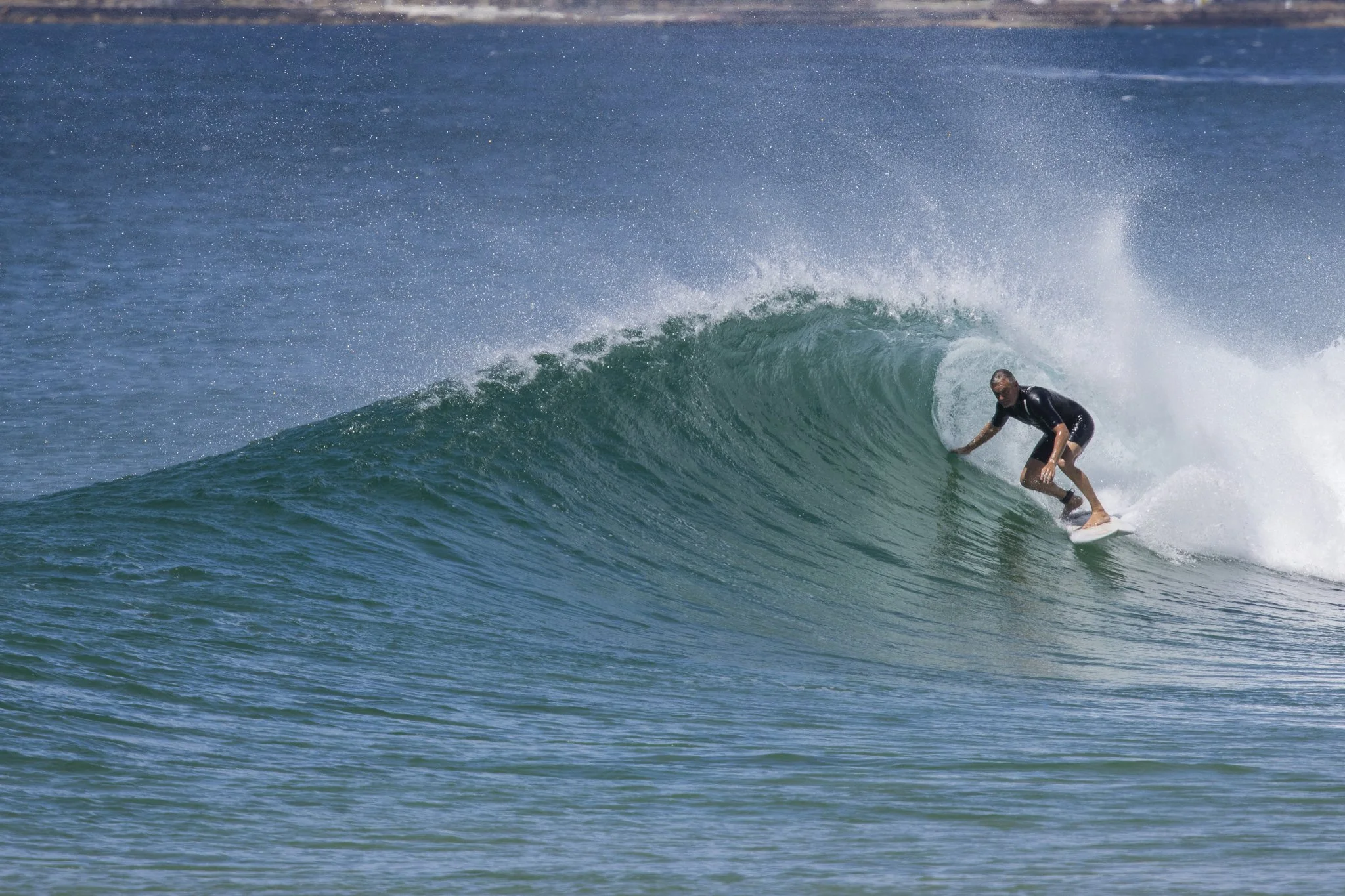 A man surfing on a large wave with a clear blue sky in the background.