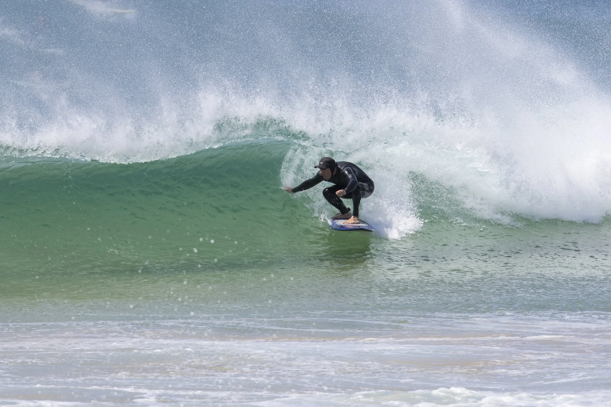 A person in a wetsuit surfing on a green wave in the ocean.