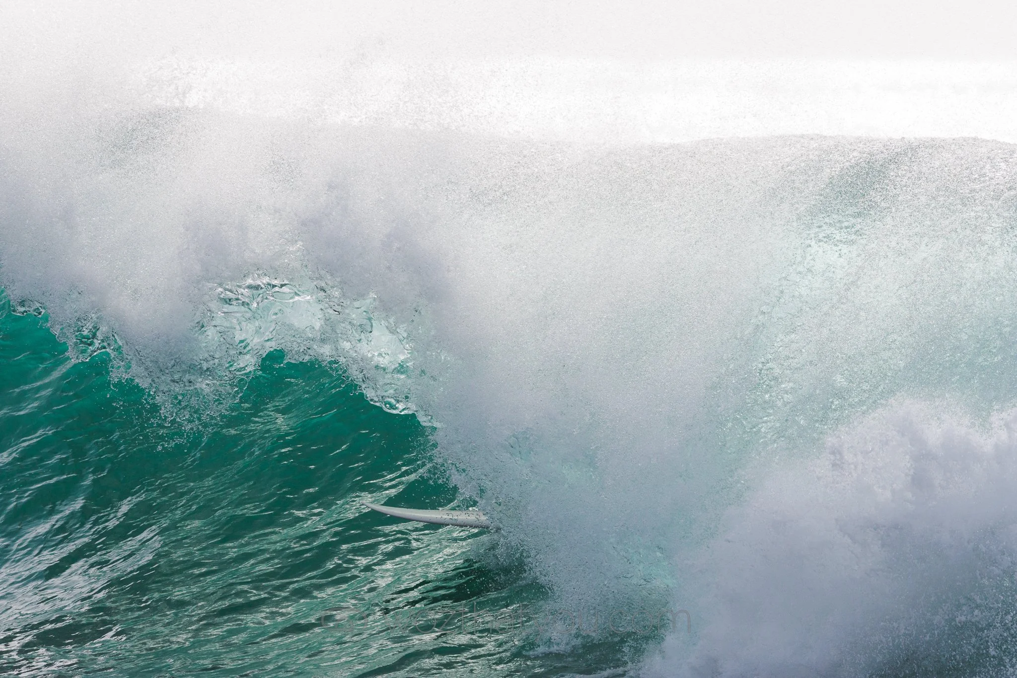 Waves crashing in the ocean with a surfboard submerged in the water.