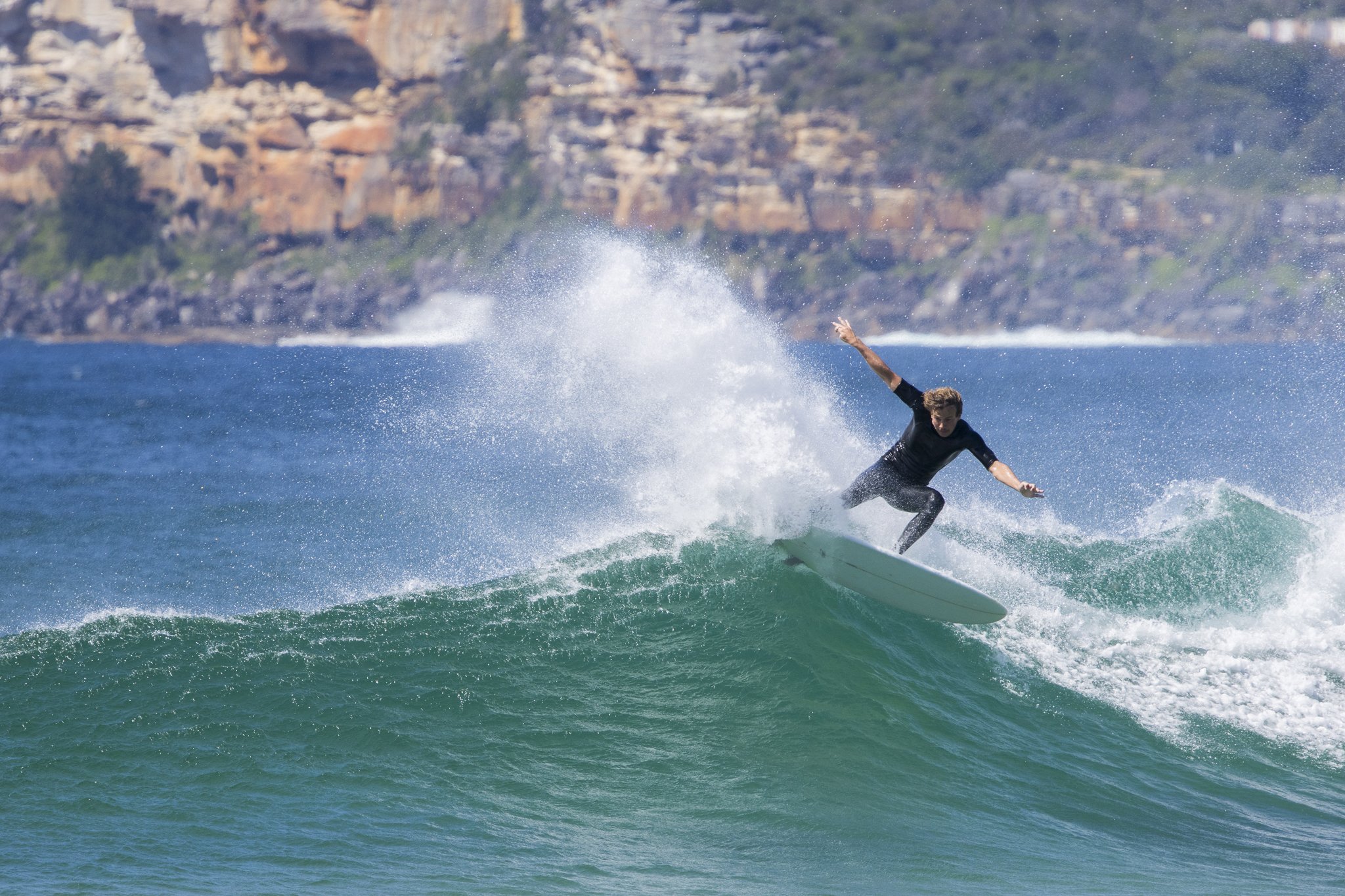 A person surfing on a wave in the ocean with cliffs in the background.