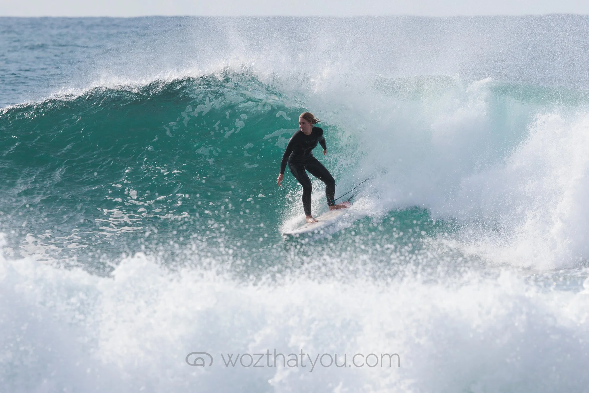 A woman in a black wetsuit surfing on a wave in the ocean.