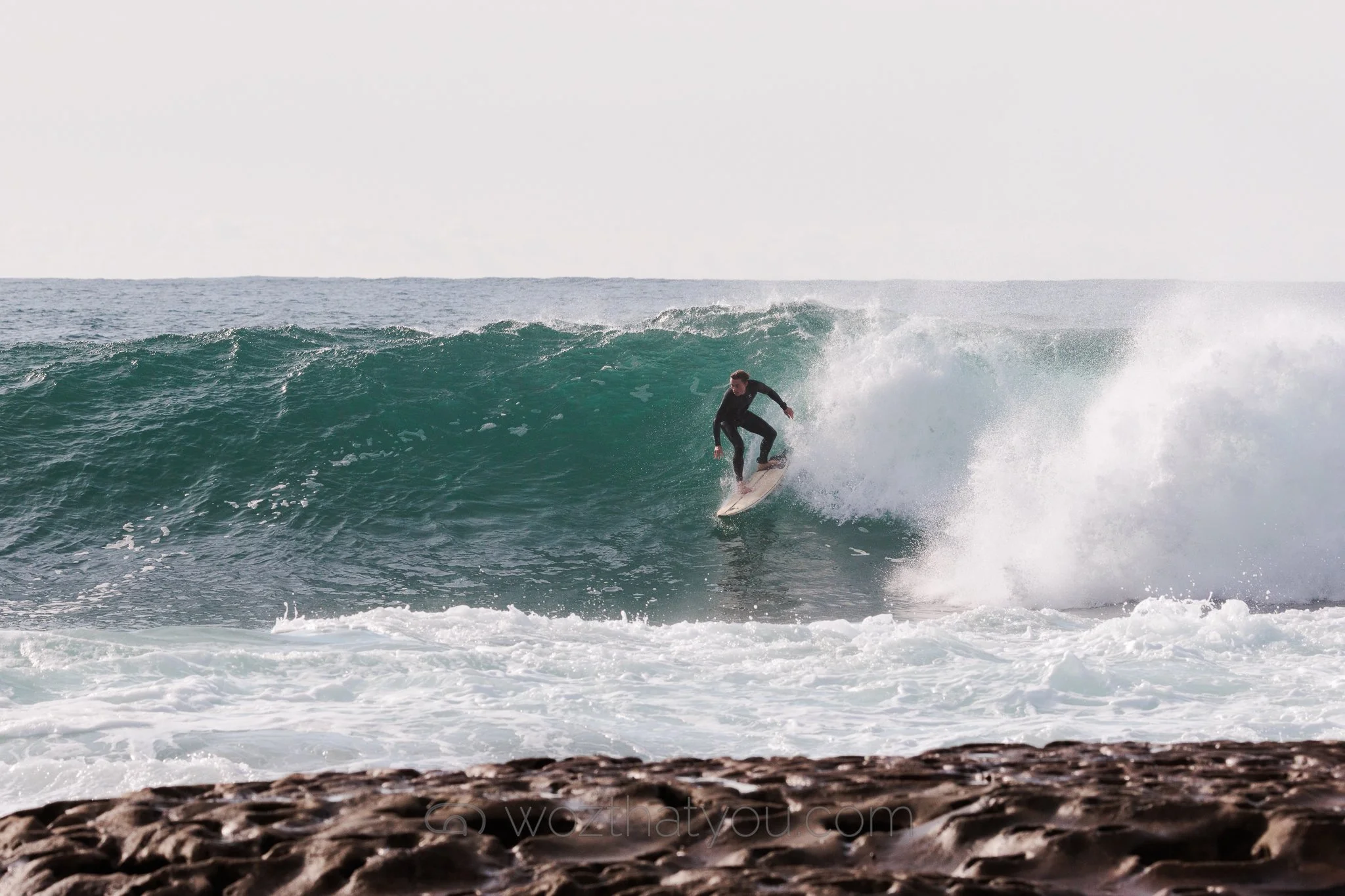 A person surfing on a wave in the ocean near the rocky shoreline.