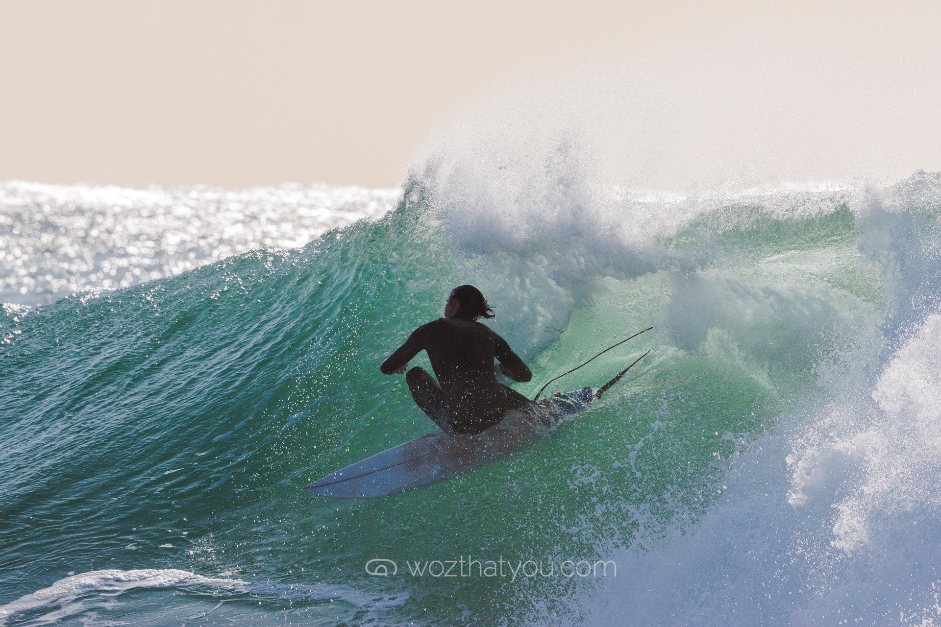 A person in a black wetsuit riding a wave on a surfboard in the ocean.