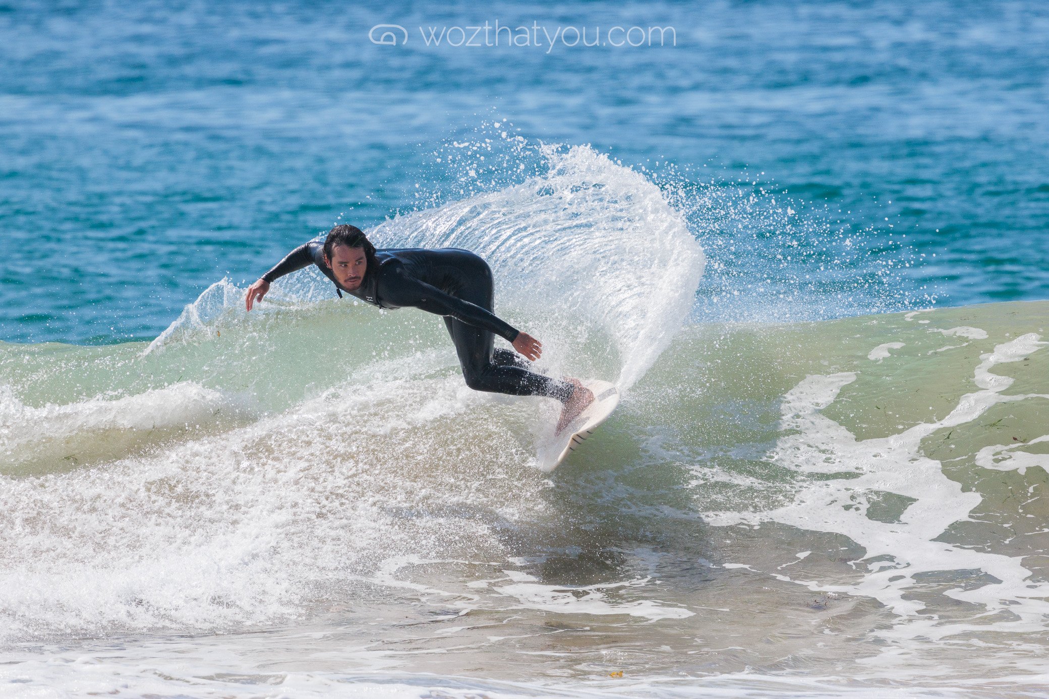 A man in a black wetsuit surfing on a wave in the ocean.