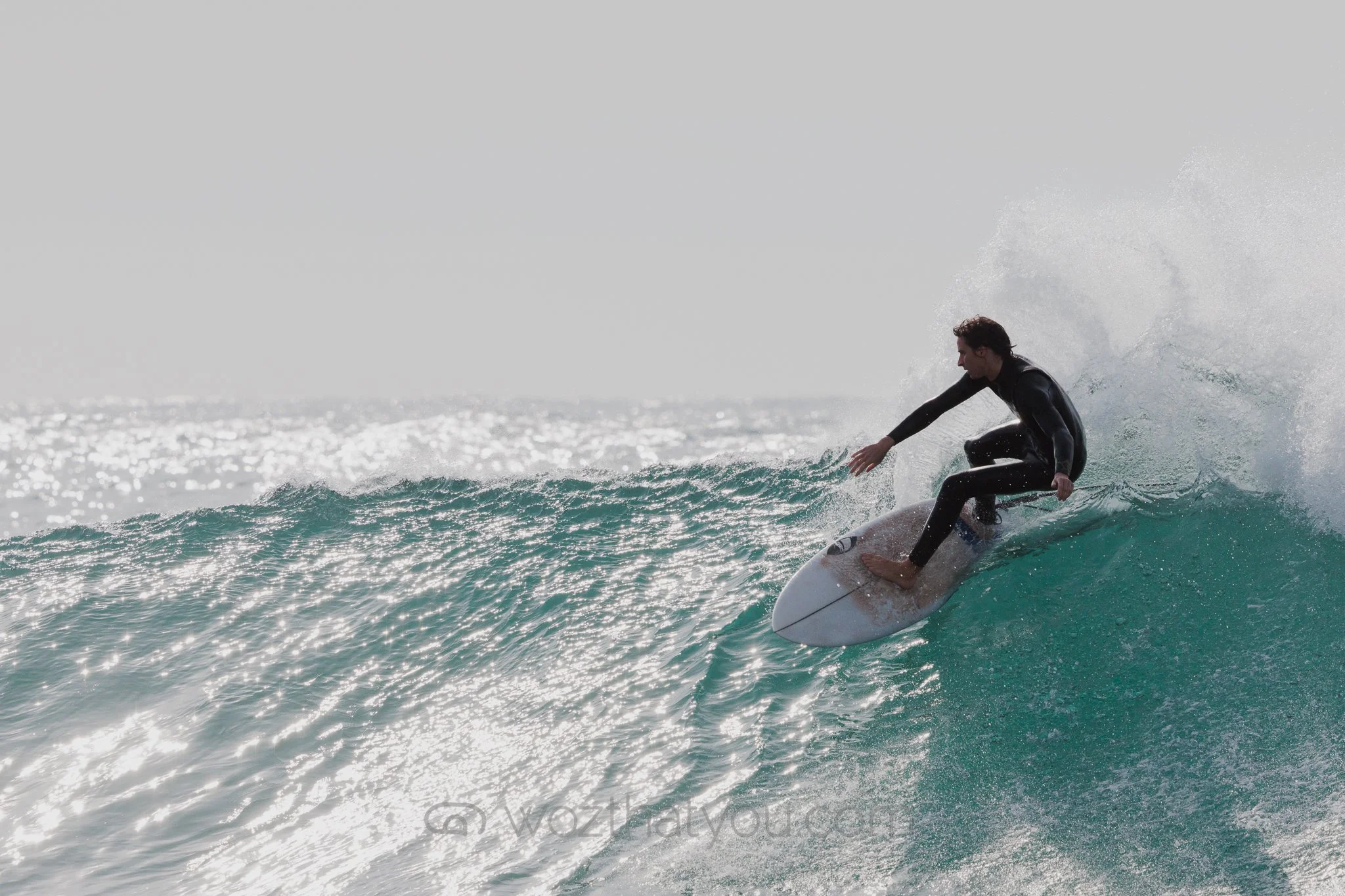 A person surfing on a wave in the ocean while wearing a wetsuit.