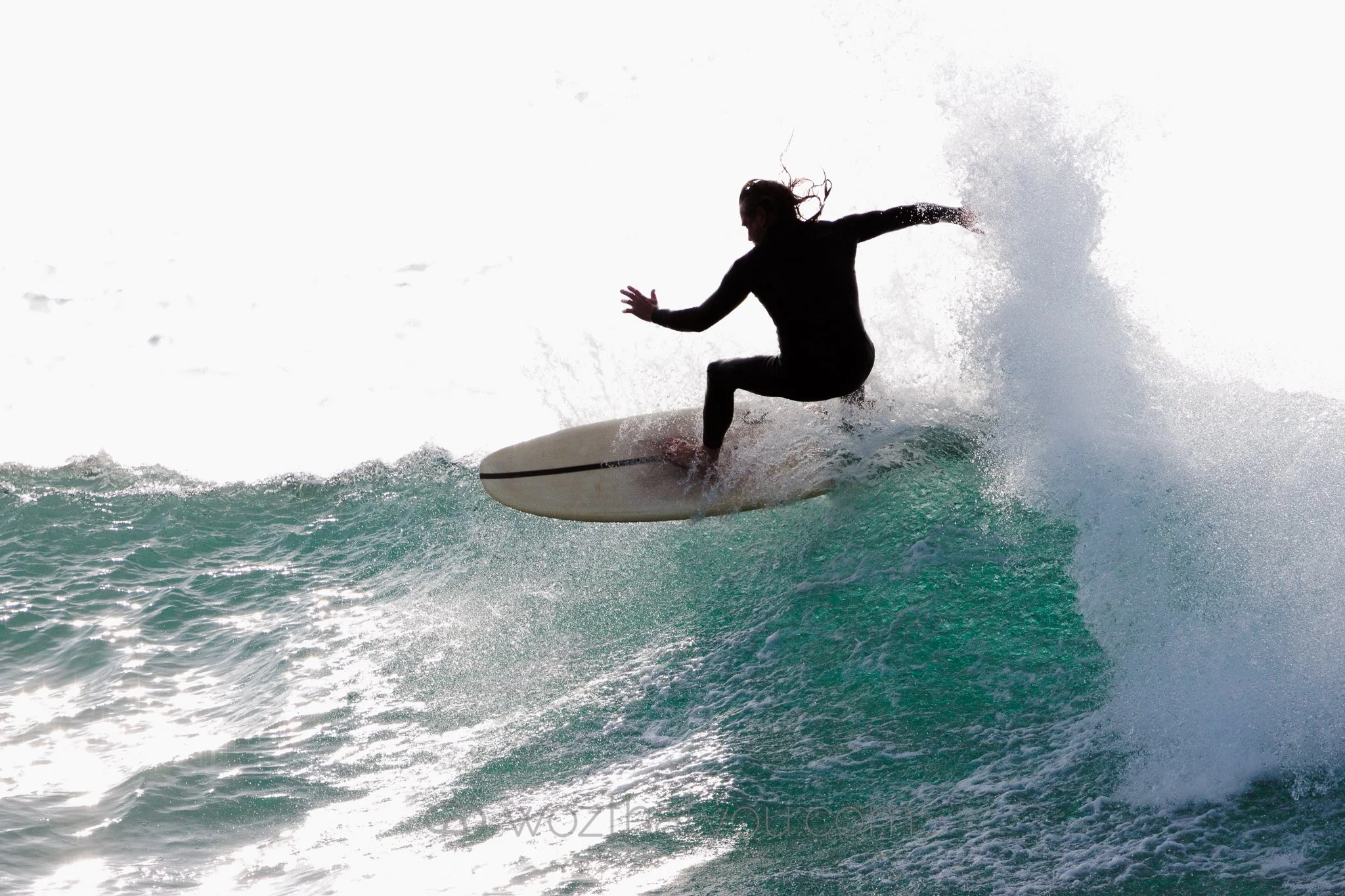 Silhouette of a woman surfing on a wave with spray.