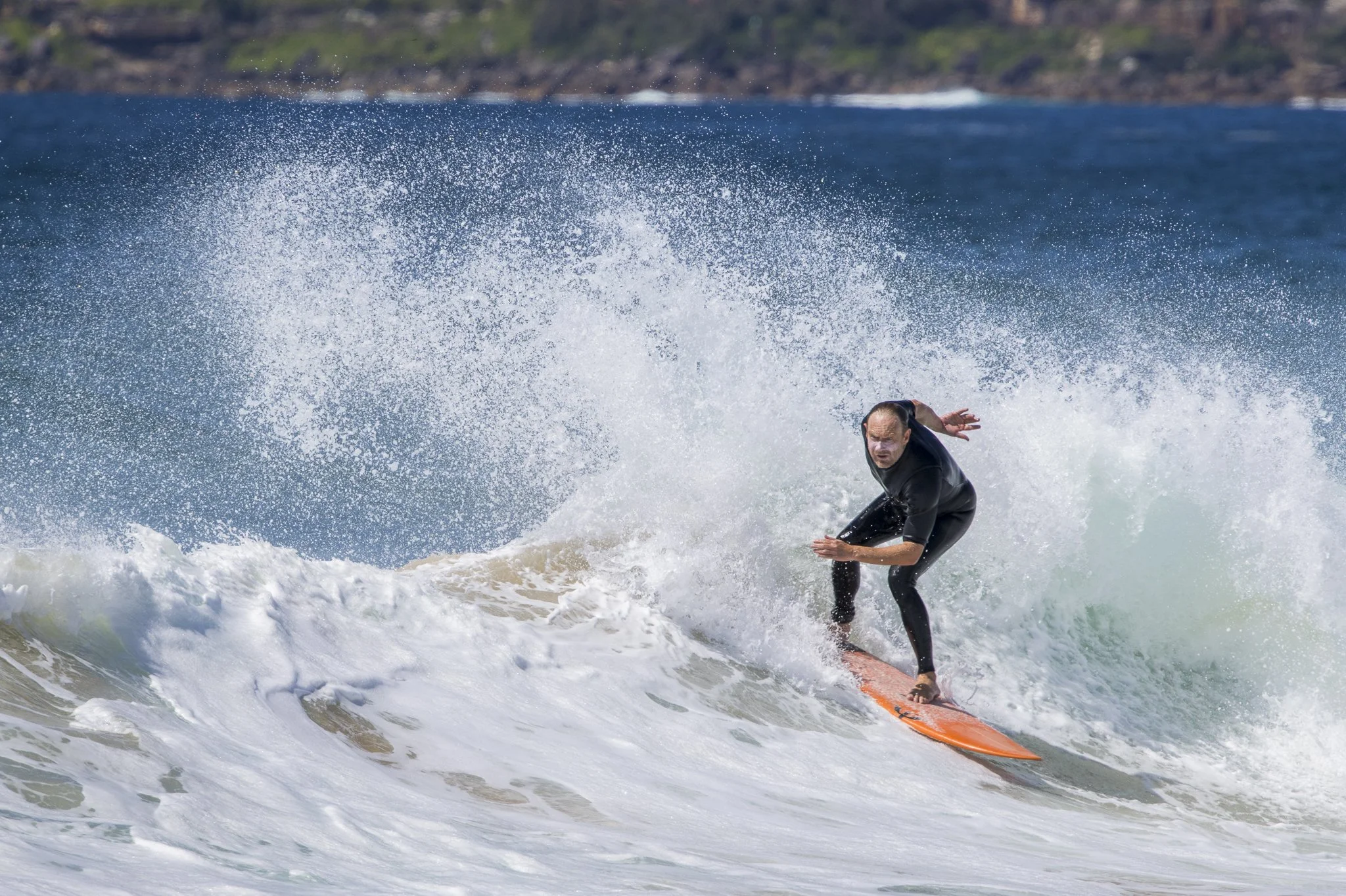 A man wearing a black wetsuit riding a wave on an orange surfboard at the beach.