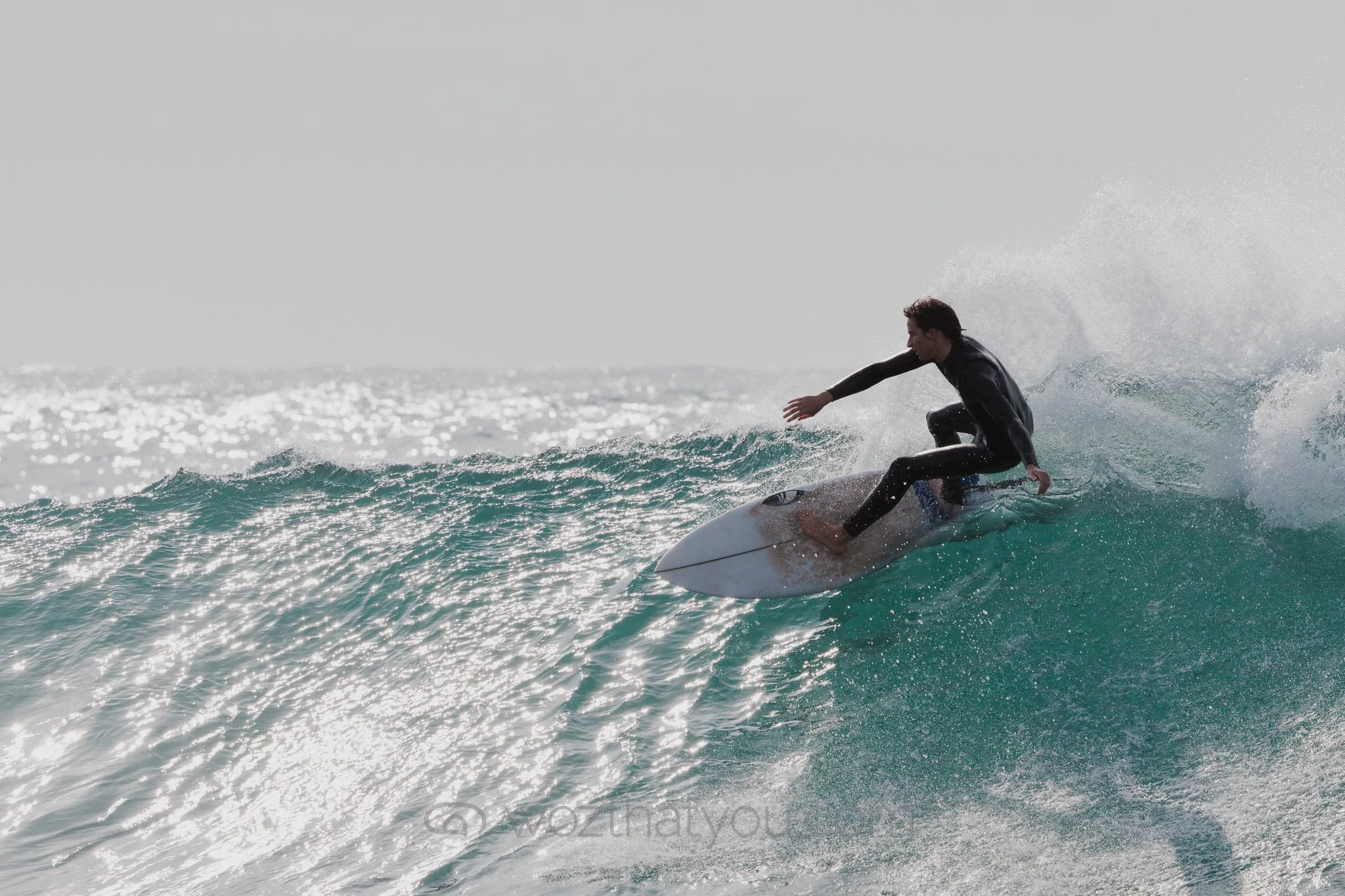 A surfer in a black wetsuit riding a wave on a surfboard in the ocean.