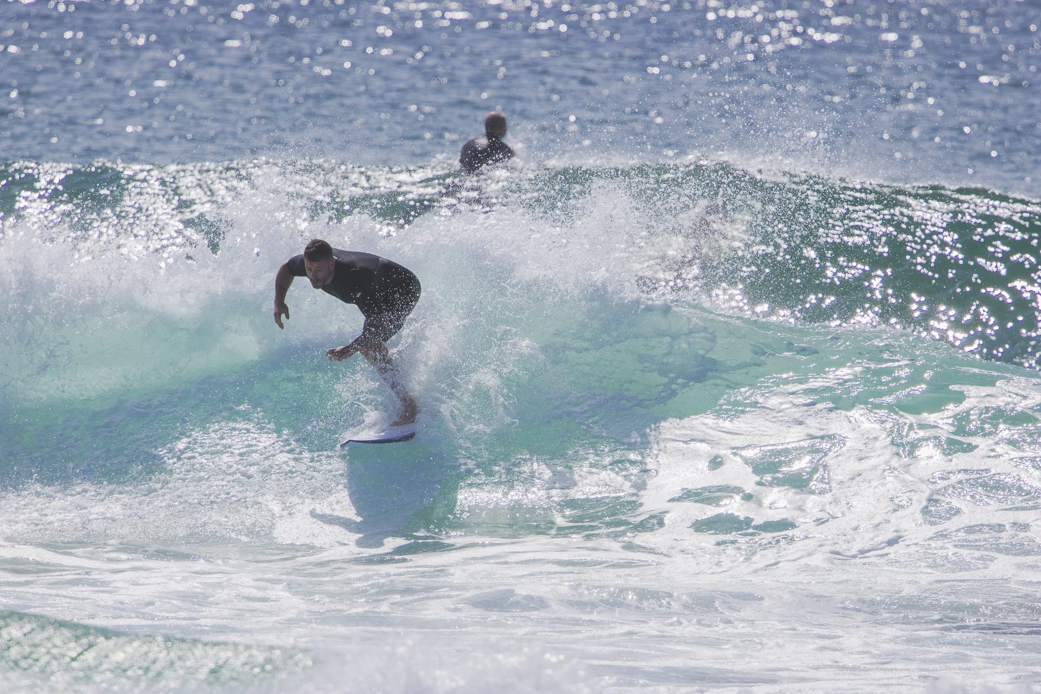 A man surfing on a wave in the ocean with another person in the background.